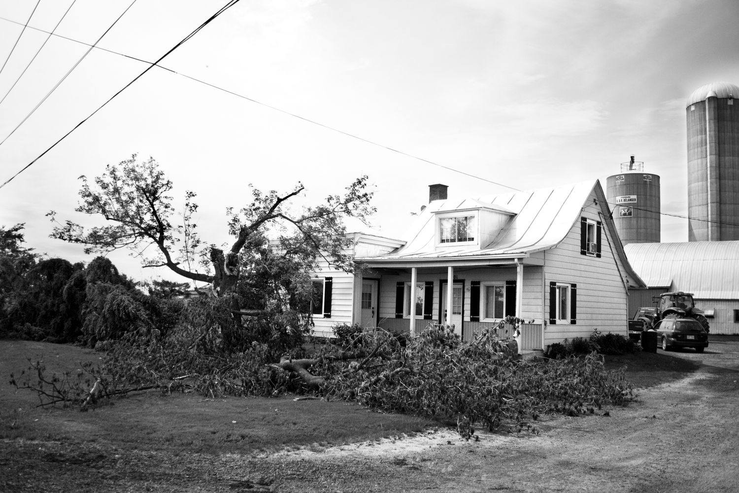 A row of white farmhouses and buildings along a rural road showing the aftermath of severe storm damage.