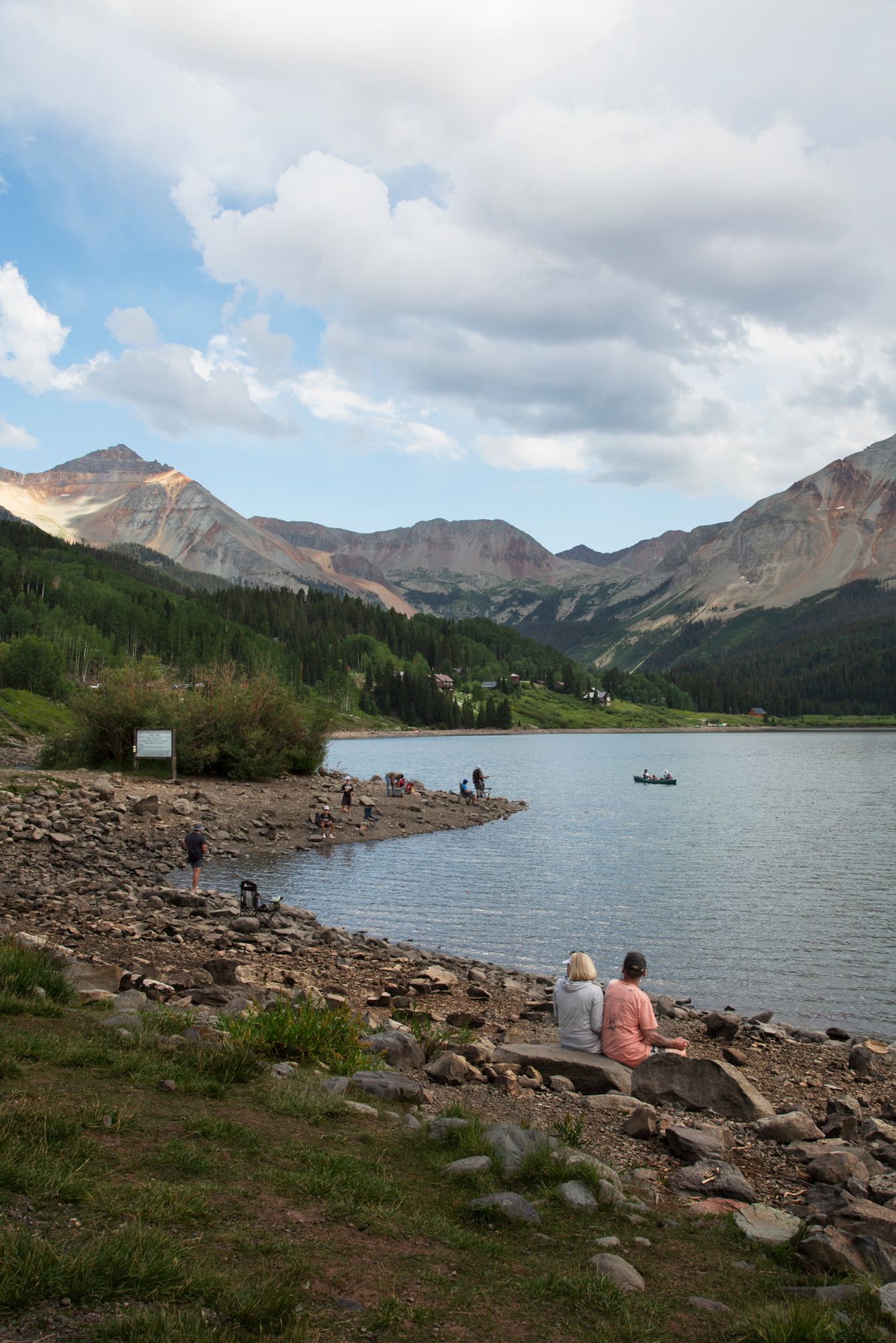 Scenic mountain lake surrounded by rugged peaks and rocky shoreline with people enjoying the peaceful wilderness views.