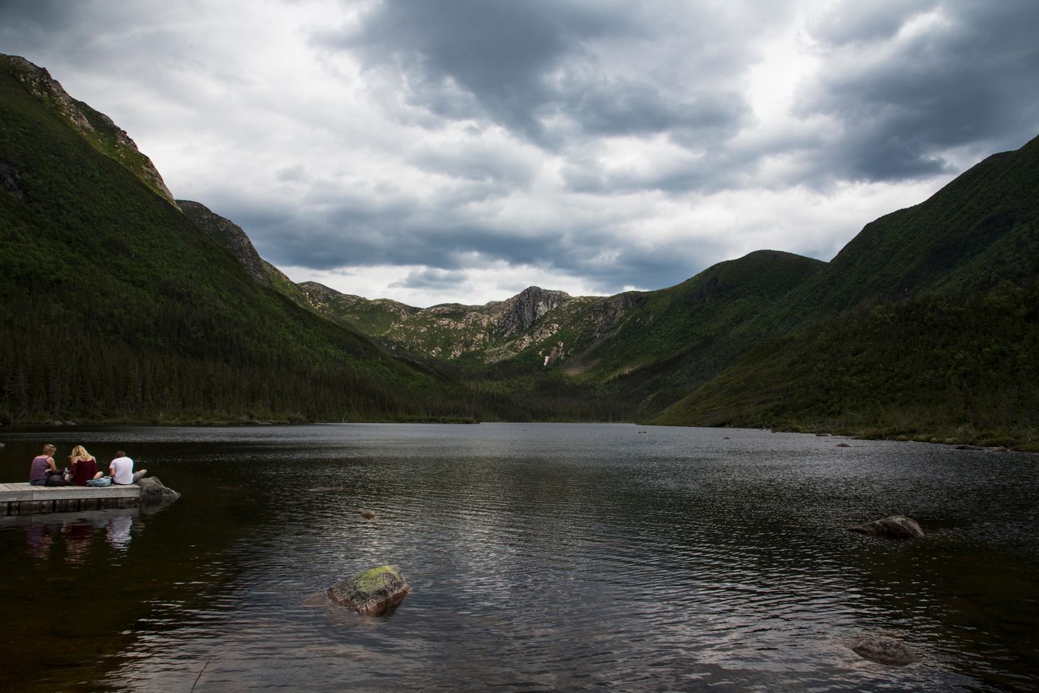 Dramatic cloudy sky over a mountain lake surrounded by steep rocky slopes.