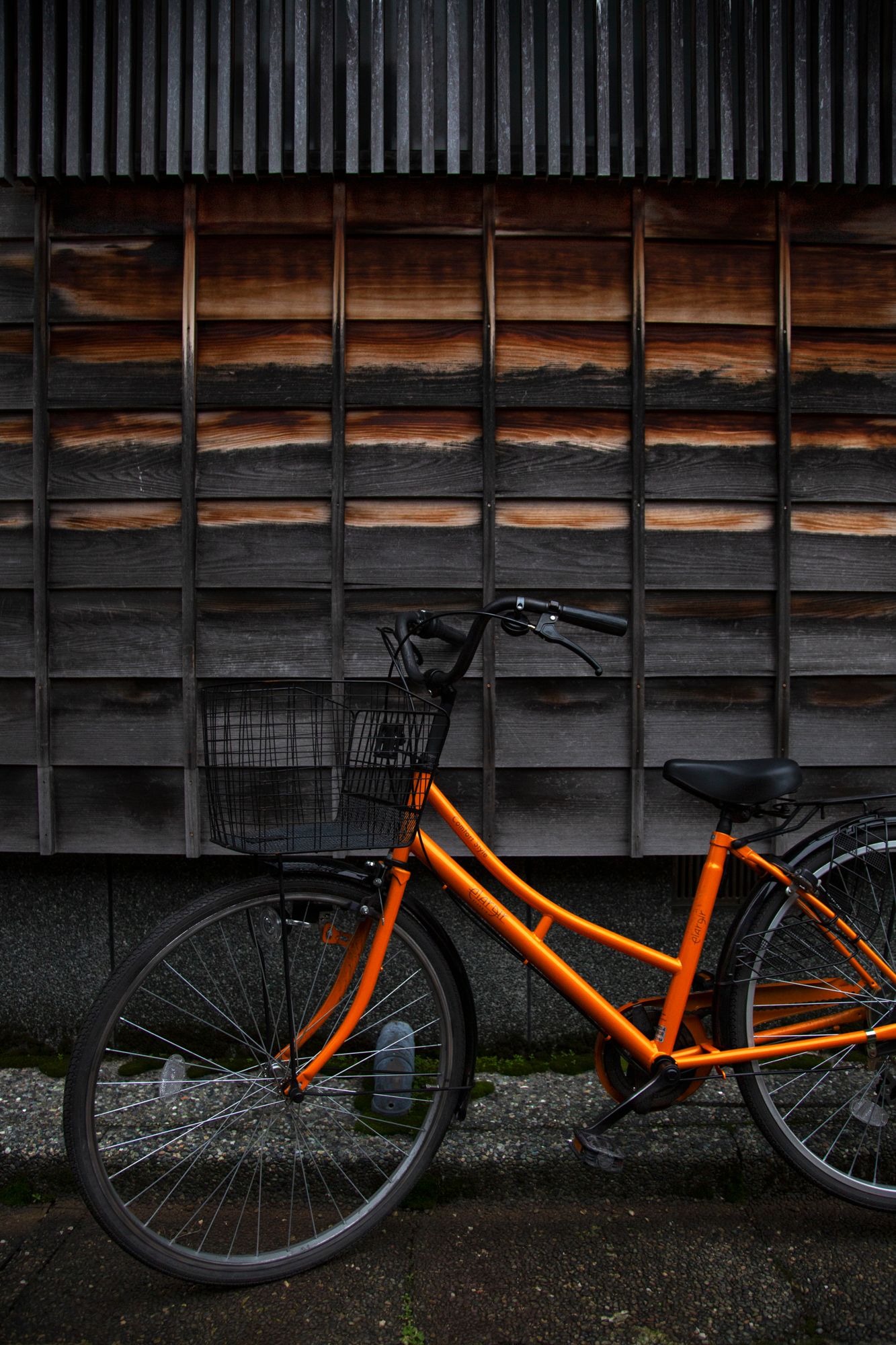 Orange bicycle frame resting against a dark wooden wall with vertical slats.