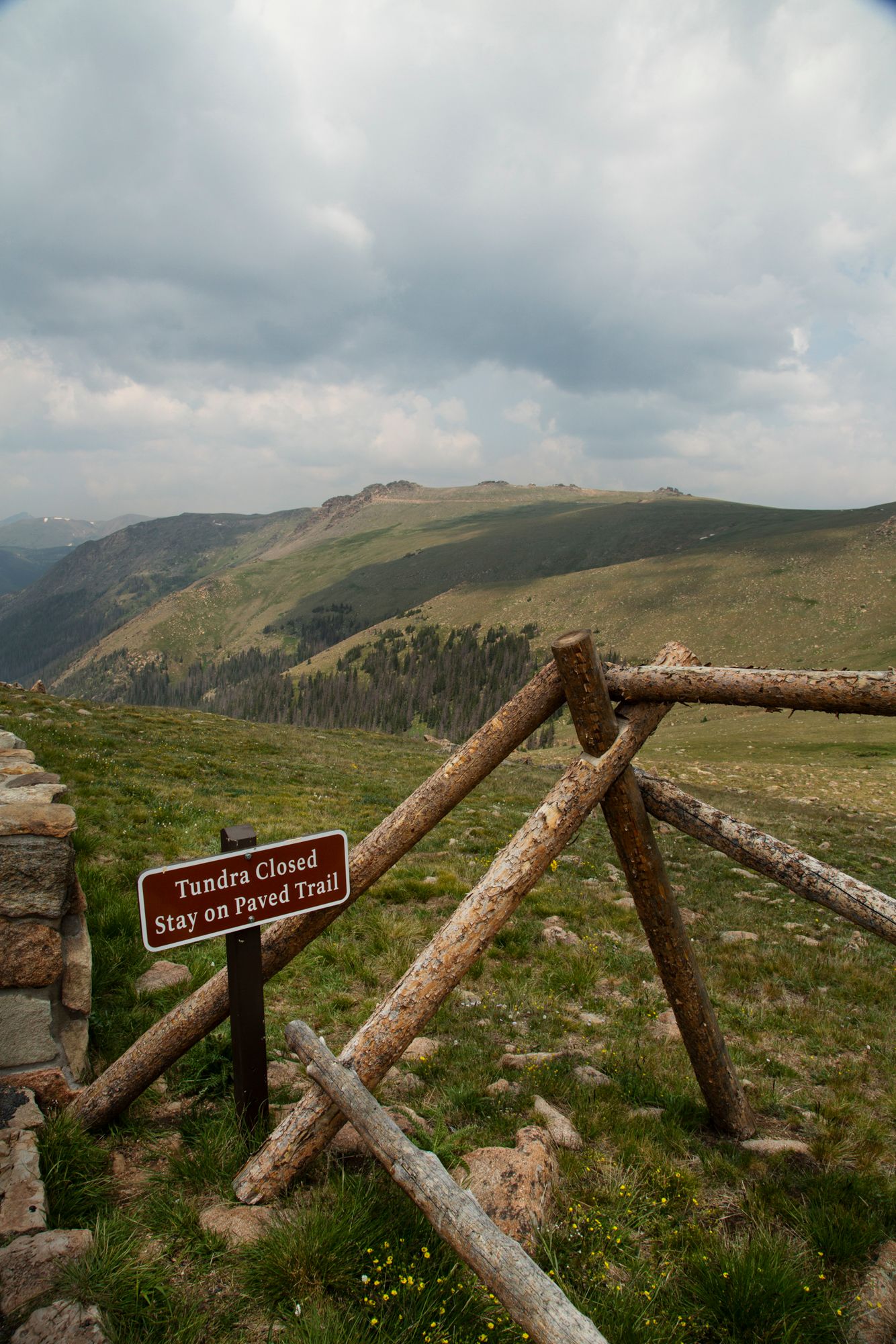 A wooden fence and 'Tundra Closed' sign mark the boundary of a hiking trail on a scenic mountain overlook.