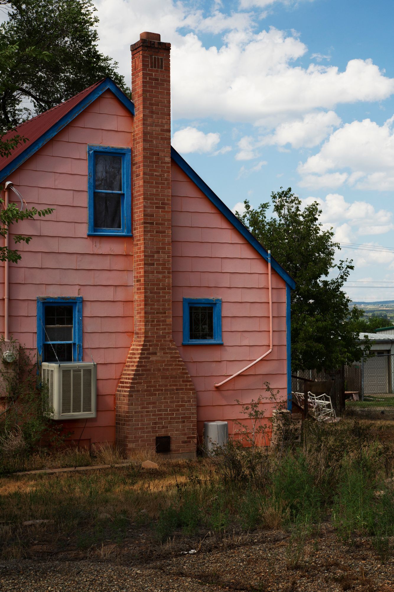 Pink house with blue trim and brick chimney shown from multiple angles against a cloudy sky and grassy landscape.