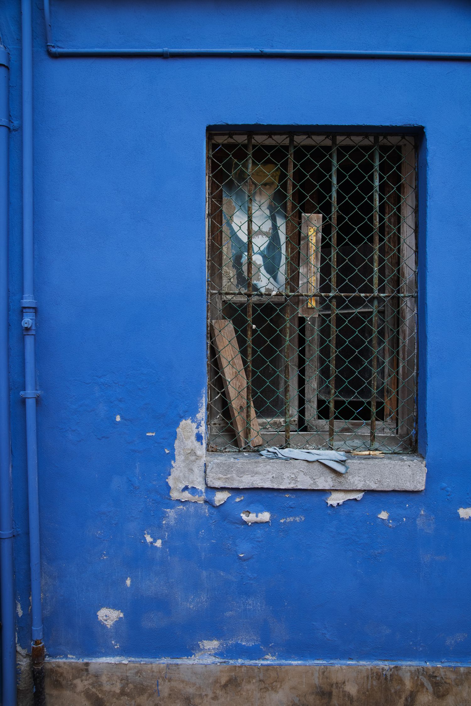 A weathered blue wall with a barred window revealing cluttered debris inside an old urban building.