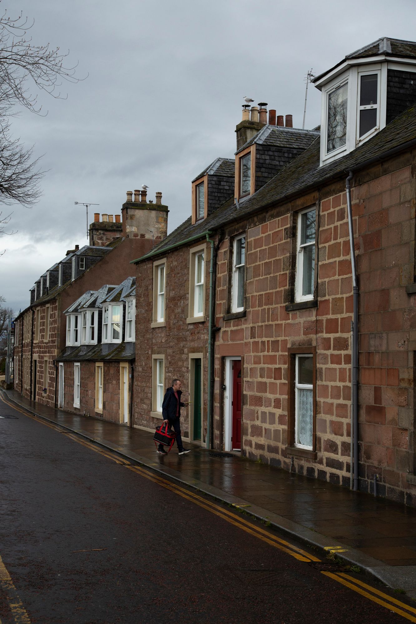 Row of traditional stone houses along a narrow street in Scotland with dormer windows and chimneys on an overcast day.