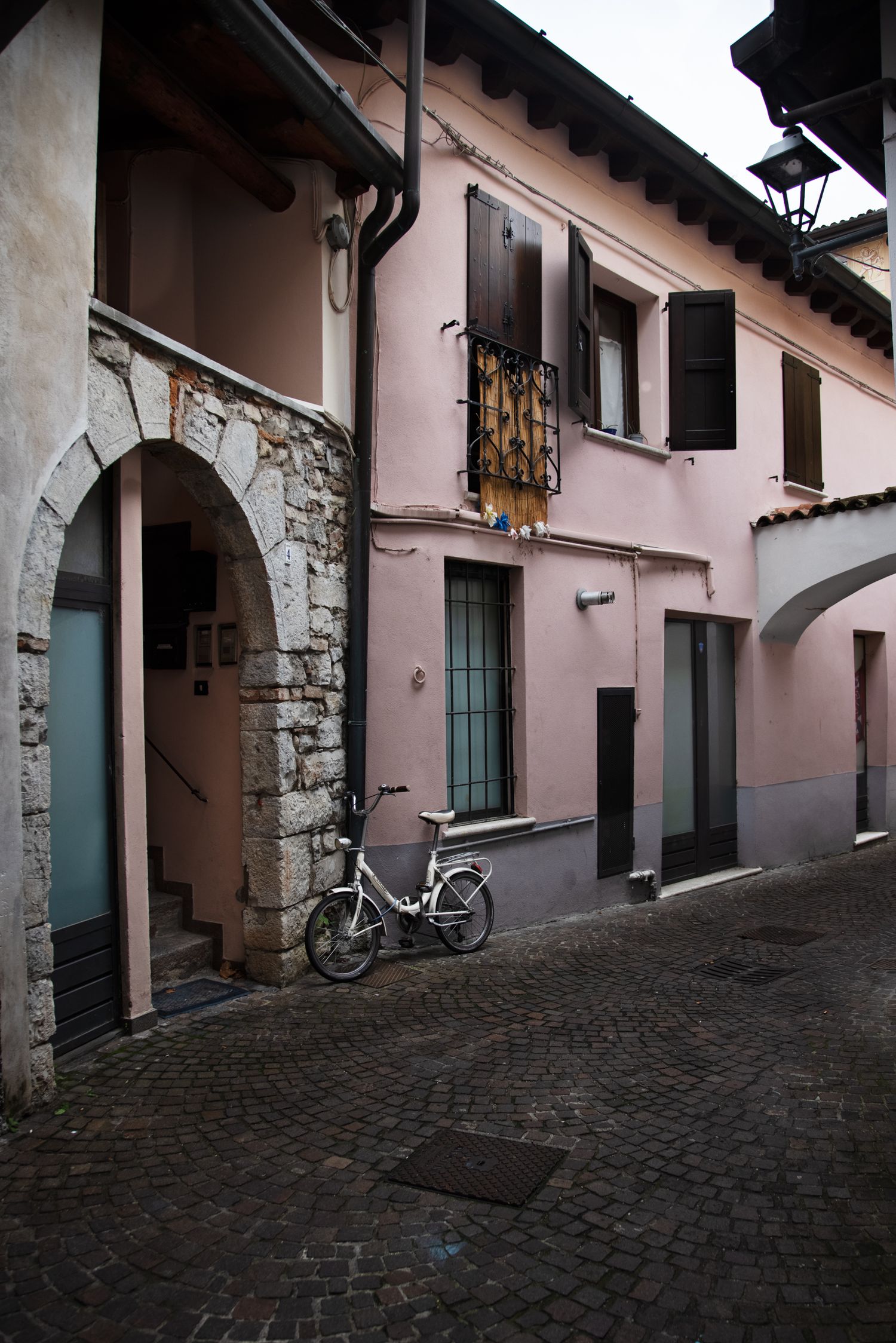 A white bicycle parked on cobblestone street beside pink building with stone arch doorway in Italian village.