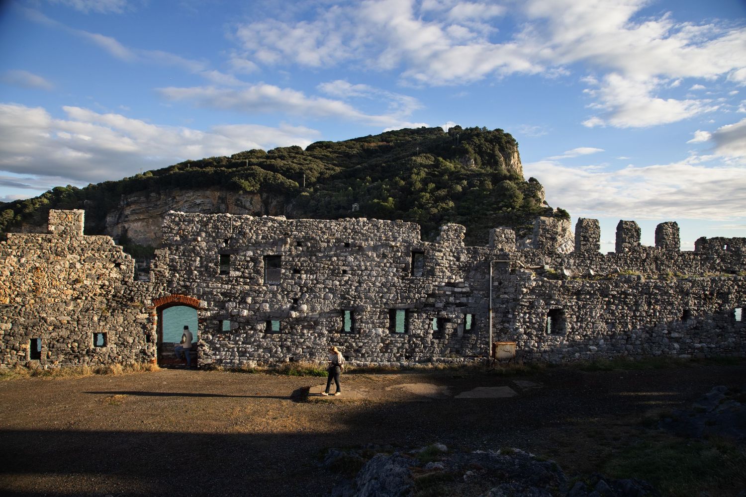 Ancient stone fortress ruins with arched entrance illuminated by golden sunset light against cloudy sky.