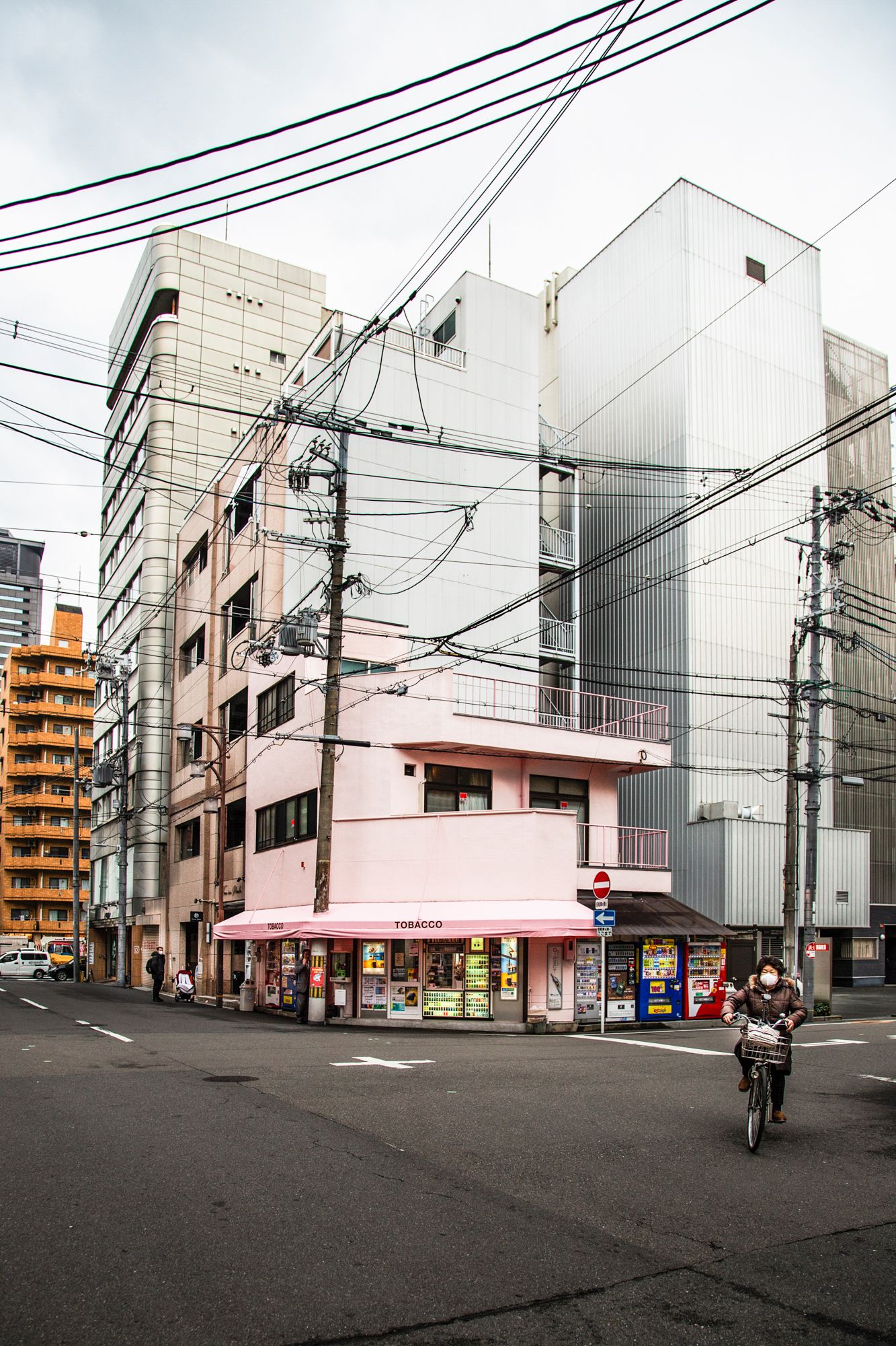 Urban street corner in Japan with pink buildings and power lines against an overcast sky.