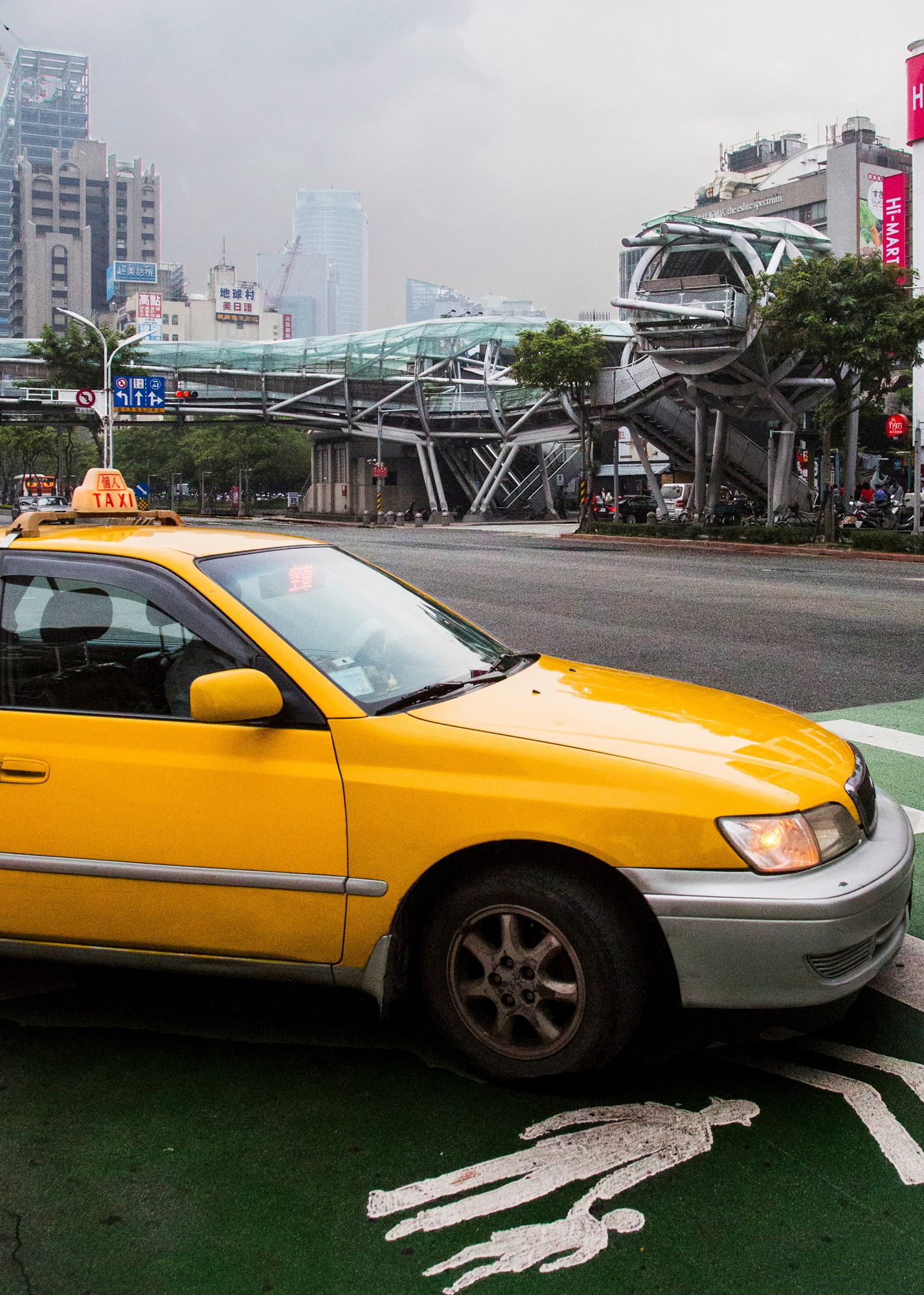 A yellow taxi cab parked near an urban city street with tall buildings in the background.