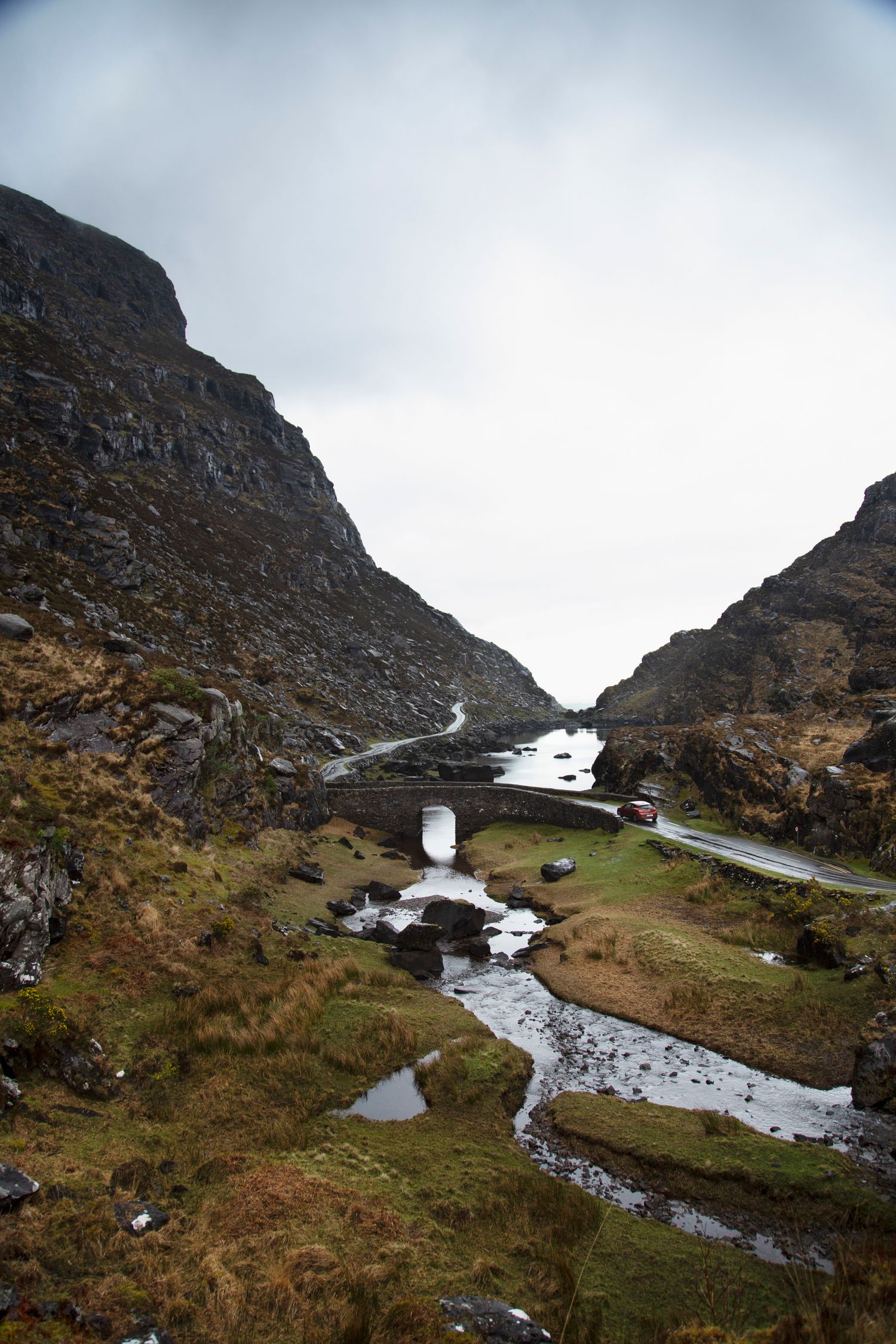 Mountain pass road winds through rocky terrain with streams flowing alongside the pathway.