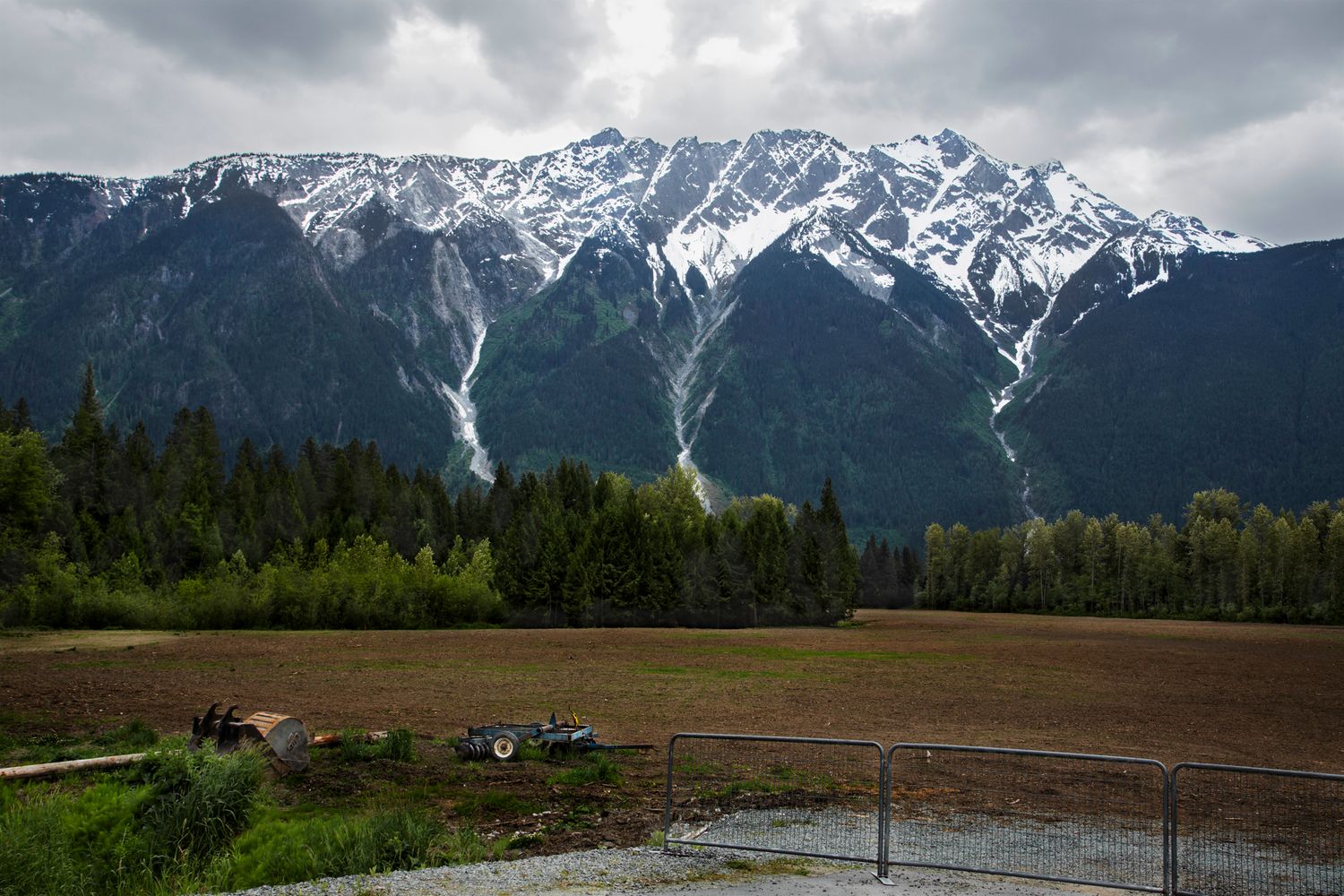 Snow-capped mountain range with dramatic waterfall visible through evergreen forest.