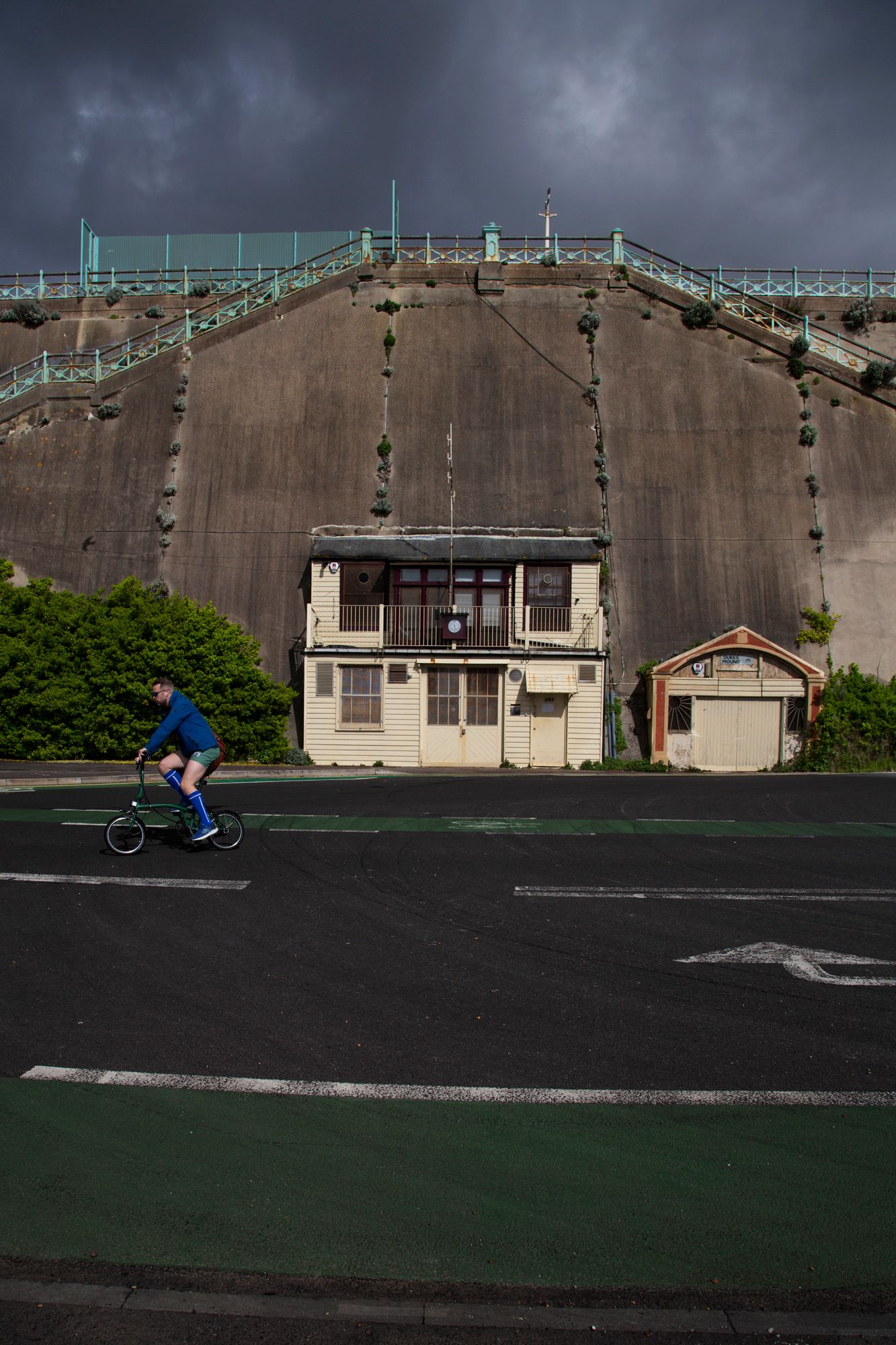 Long concrete wall with sports court and buildings under dark stormy skies.