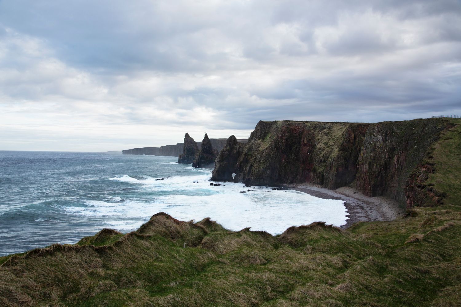 Dramatic coastal cliffs and rugged shoreline of Scotland's Duncansby Head under moody cloudy skies.