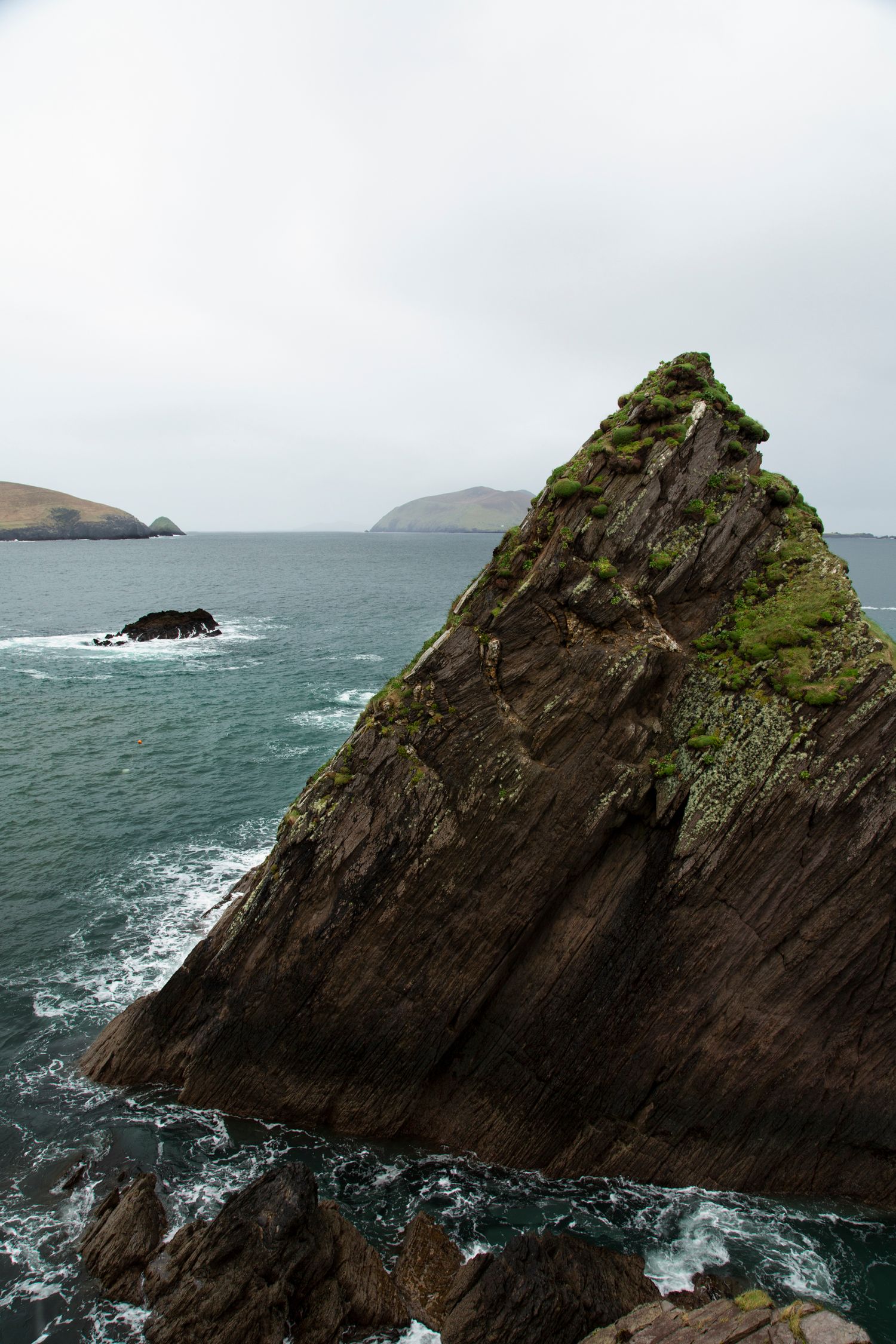 Dramatic rocky cliffs jutting into a stormy sea with distant islands in view.
