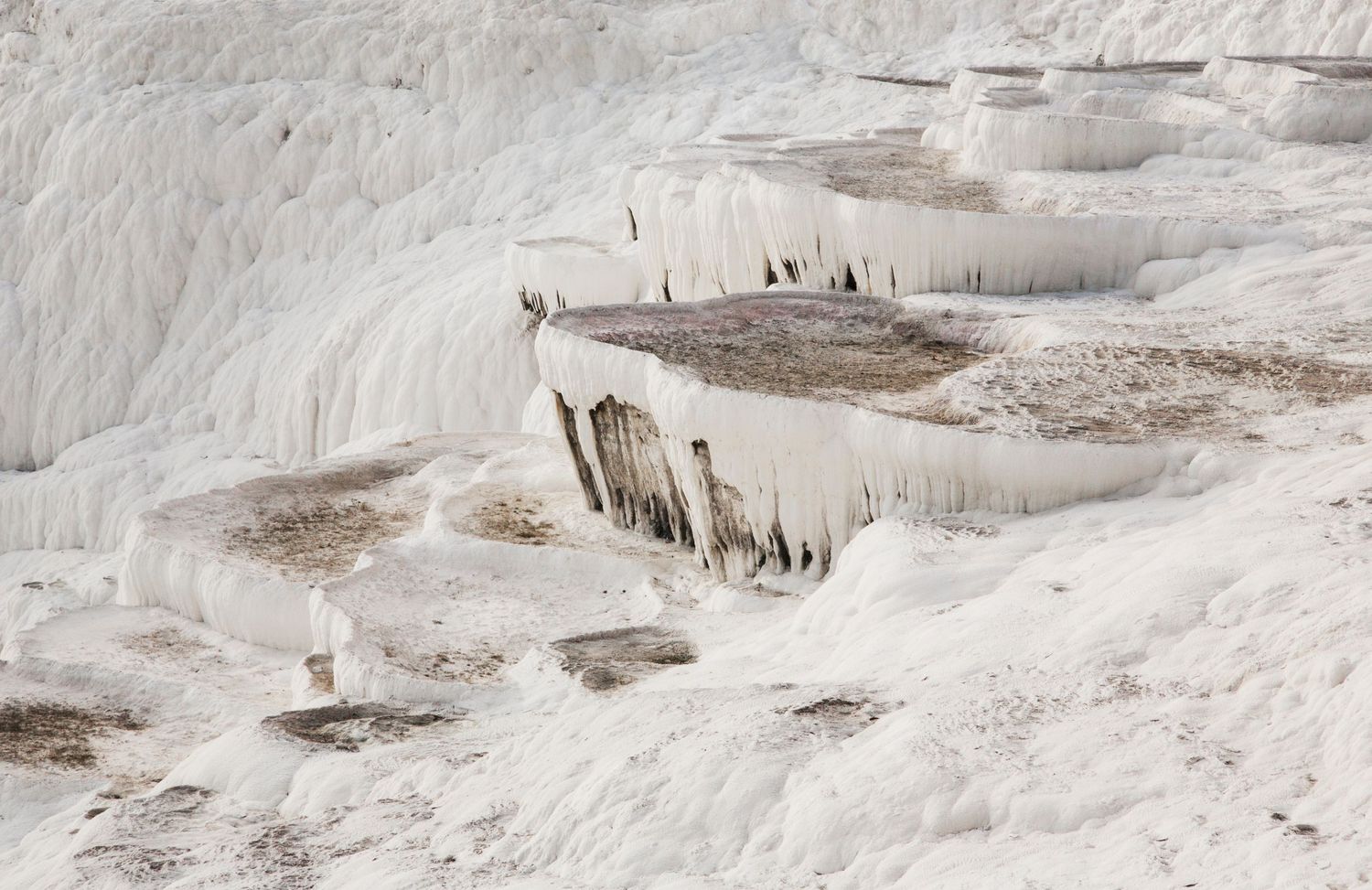 Icy white mineral formations cover a hillside with small figures visible in the distance.