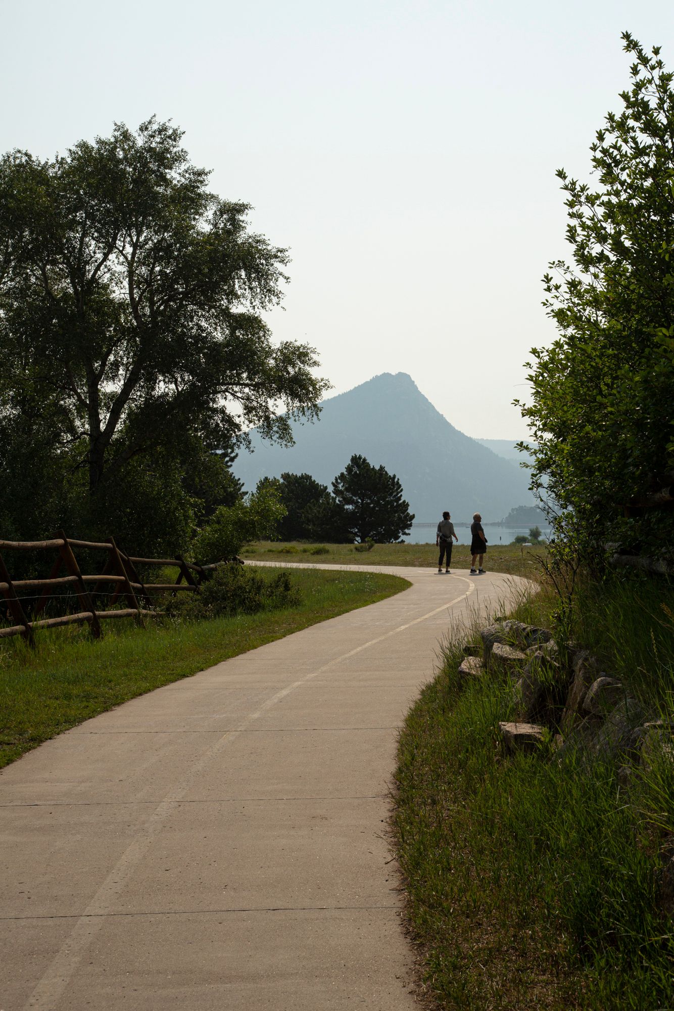 A winding paved path through green vegetation leads to distant mountains silhouetted against the sky.