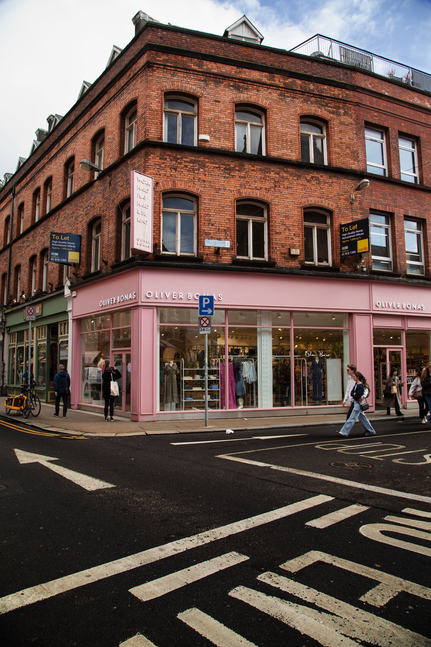 Red brick commercial buildings with a pink painted corner shop and pedestrian crossings.