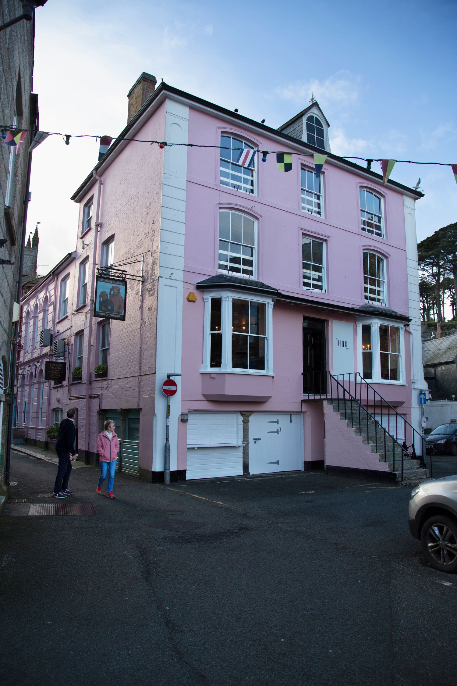 Pink Victorian-style corner building with white trim and multiple stories on a quiet street.