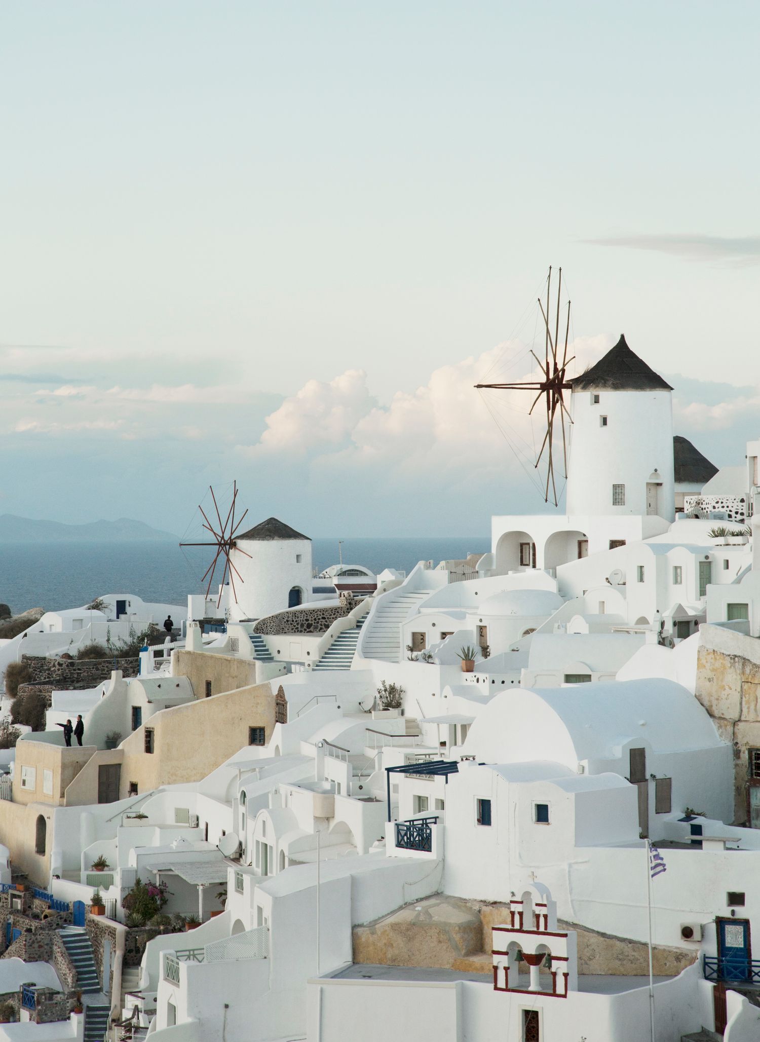 Classic Santorini landscape with white windmills and cubic buildings against a bright blue sky.