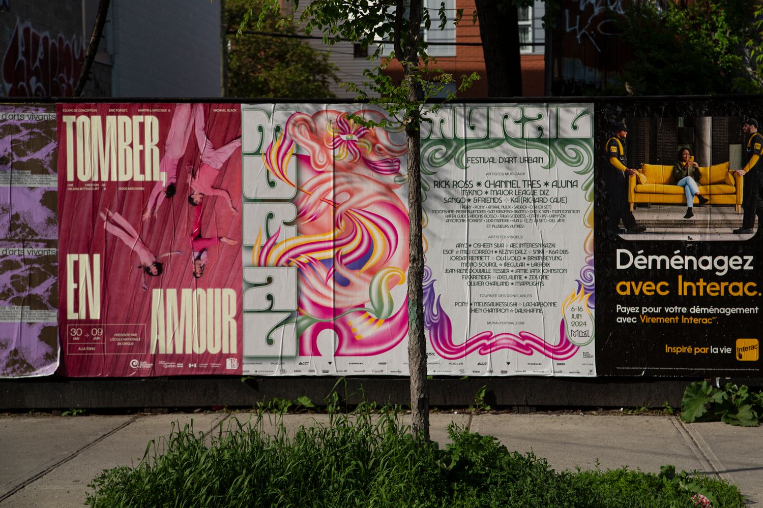 Long wall covered in pink and purple street art murals along an urban sidewalk.