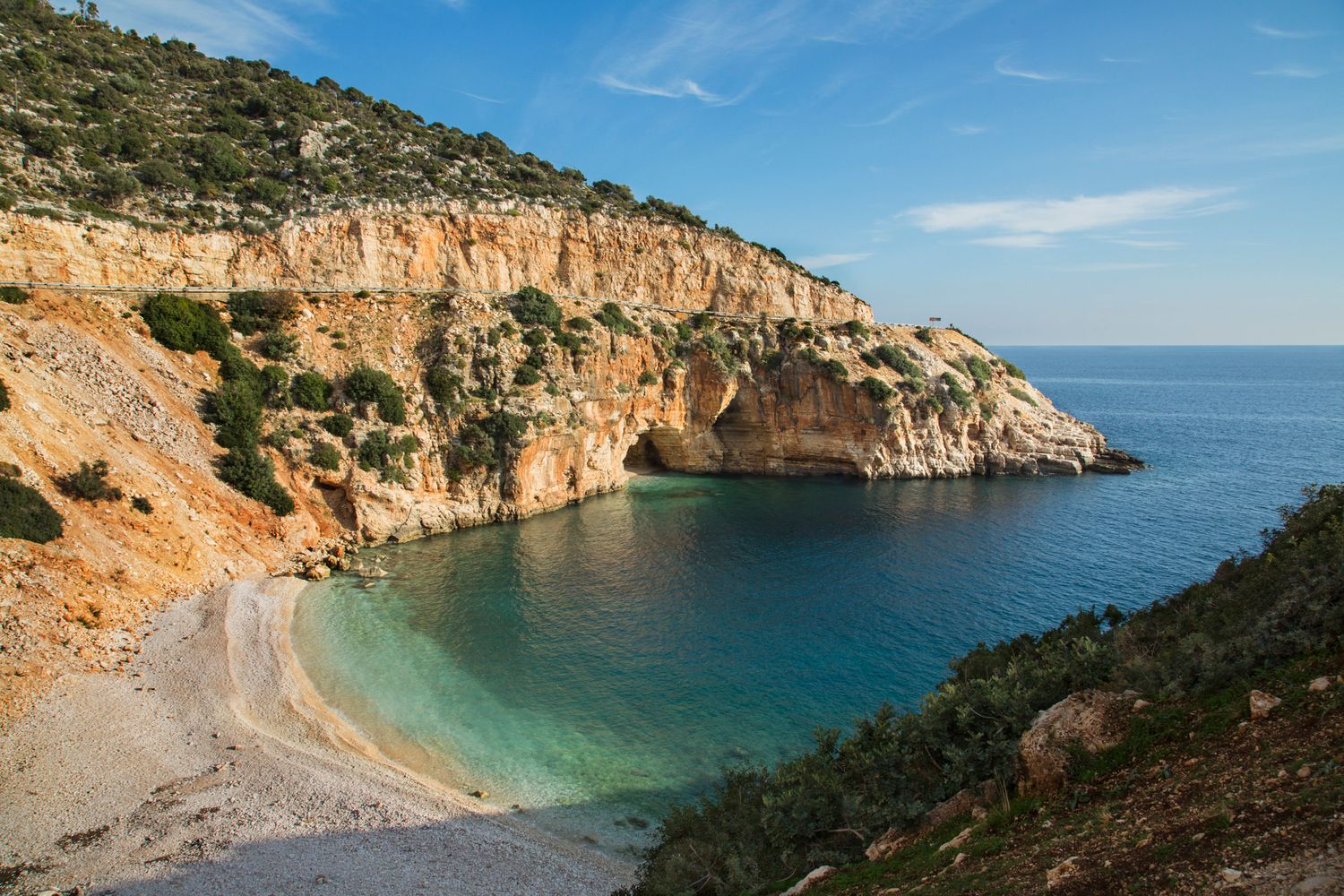 Secluded Mediterranean cove with turquoise waters surrounded by rocky orange cliffs.