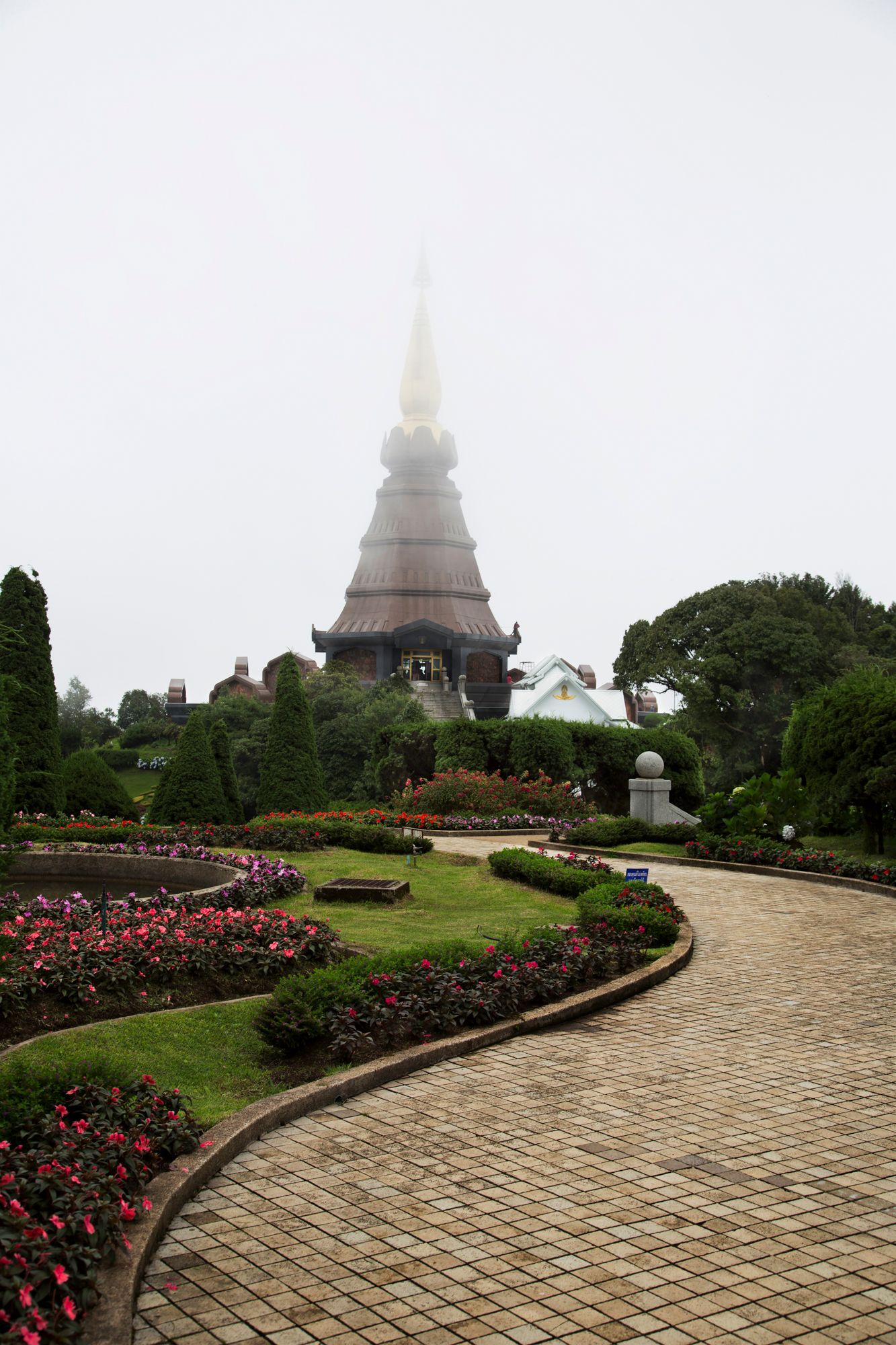 Misty temple grounds with stone pathways and rose gardens leading to pagoda structures.