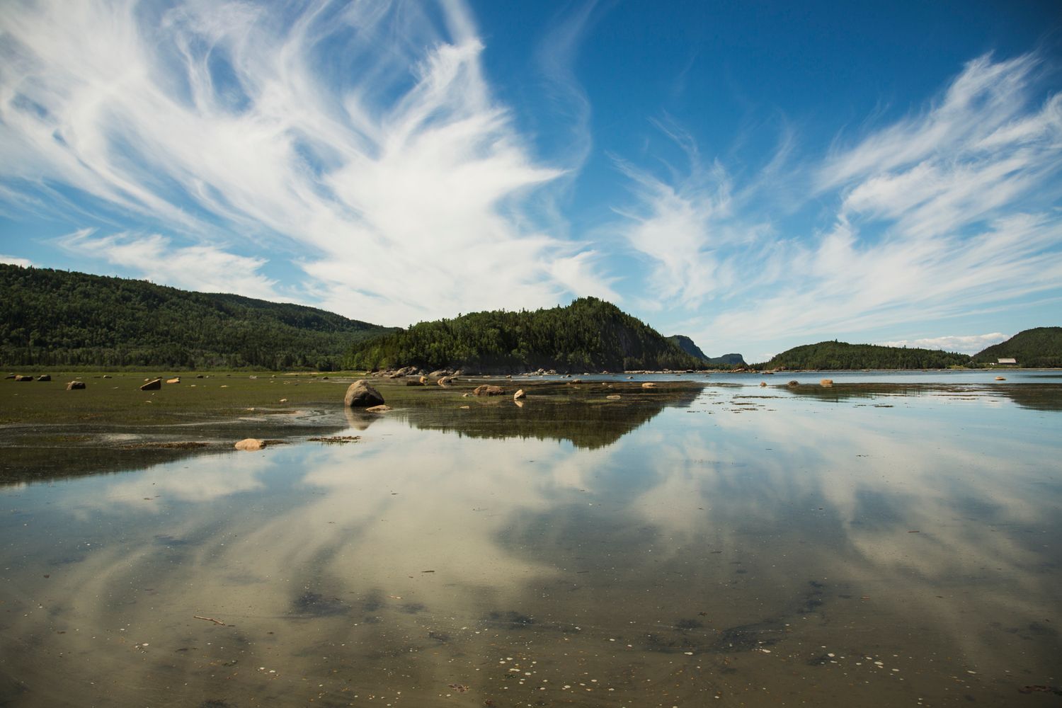 Reflective lake surface mirrors dramatic cloud formations under bright blue skies.