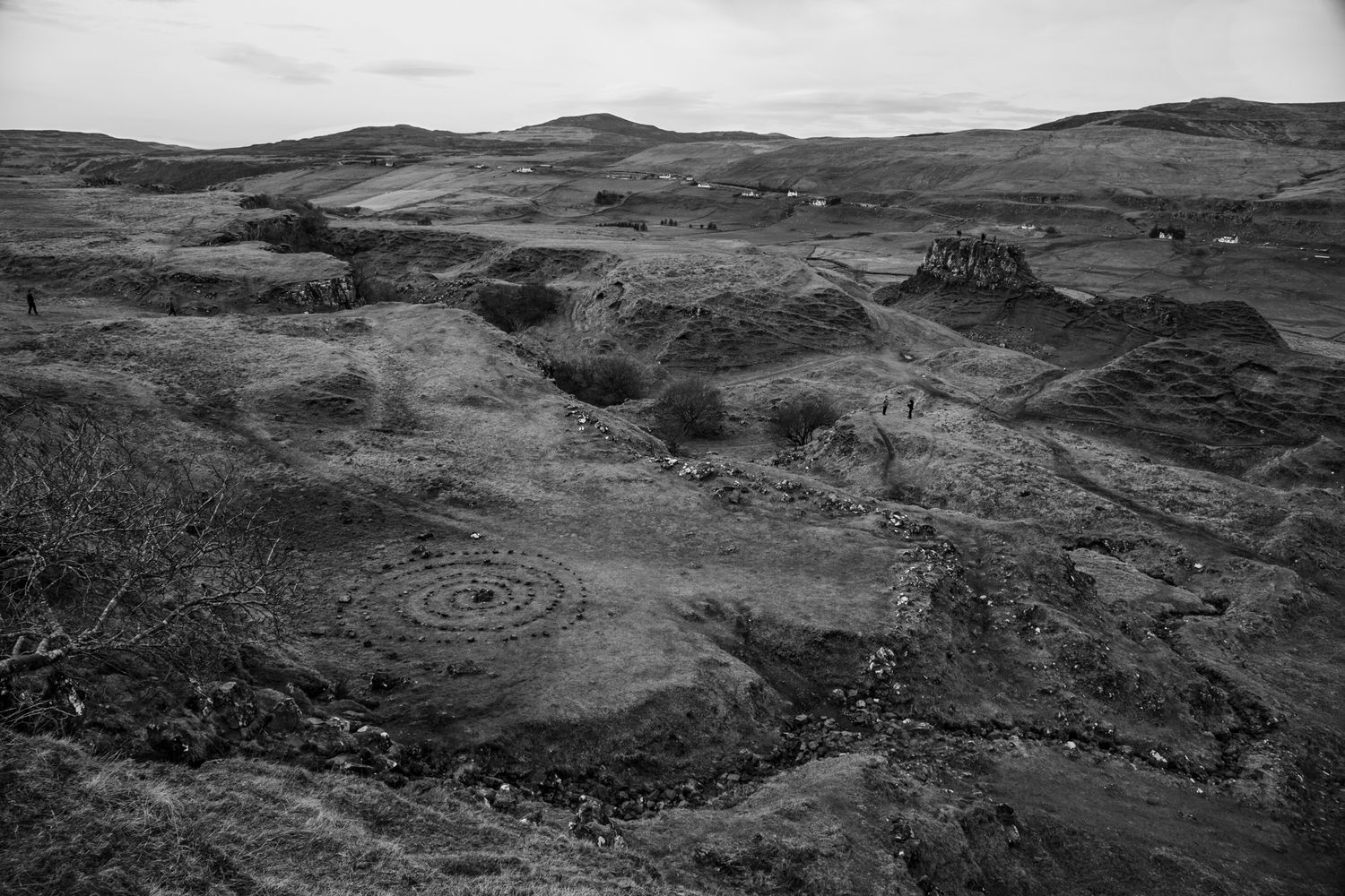 Black and white landscape of rugged mountainous terrain with winding paths through barren rocky slopes.