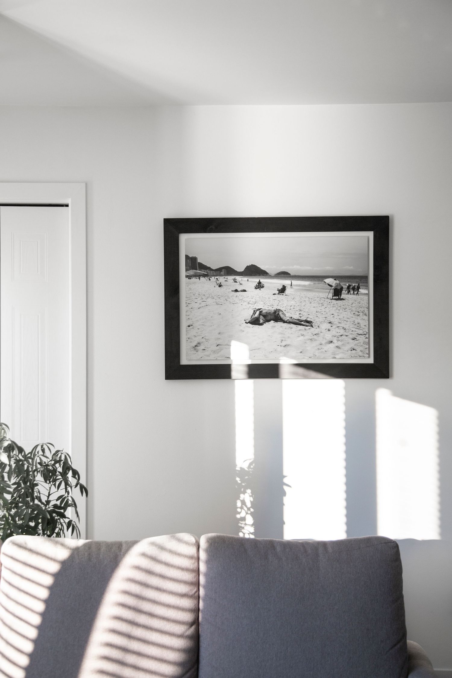 Black and white beach photo in frame casting dramatic shadows on white wall above grey couch.