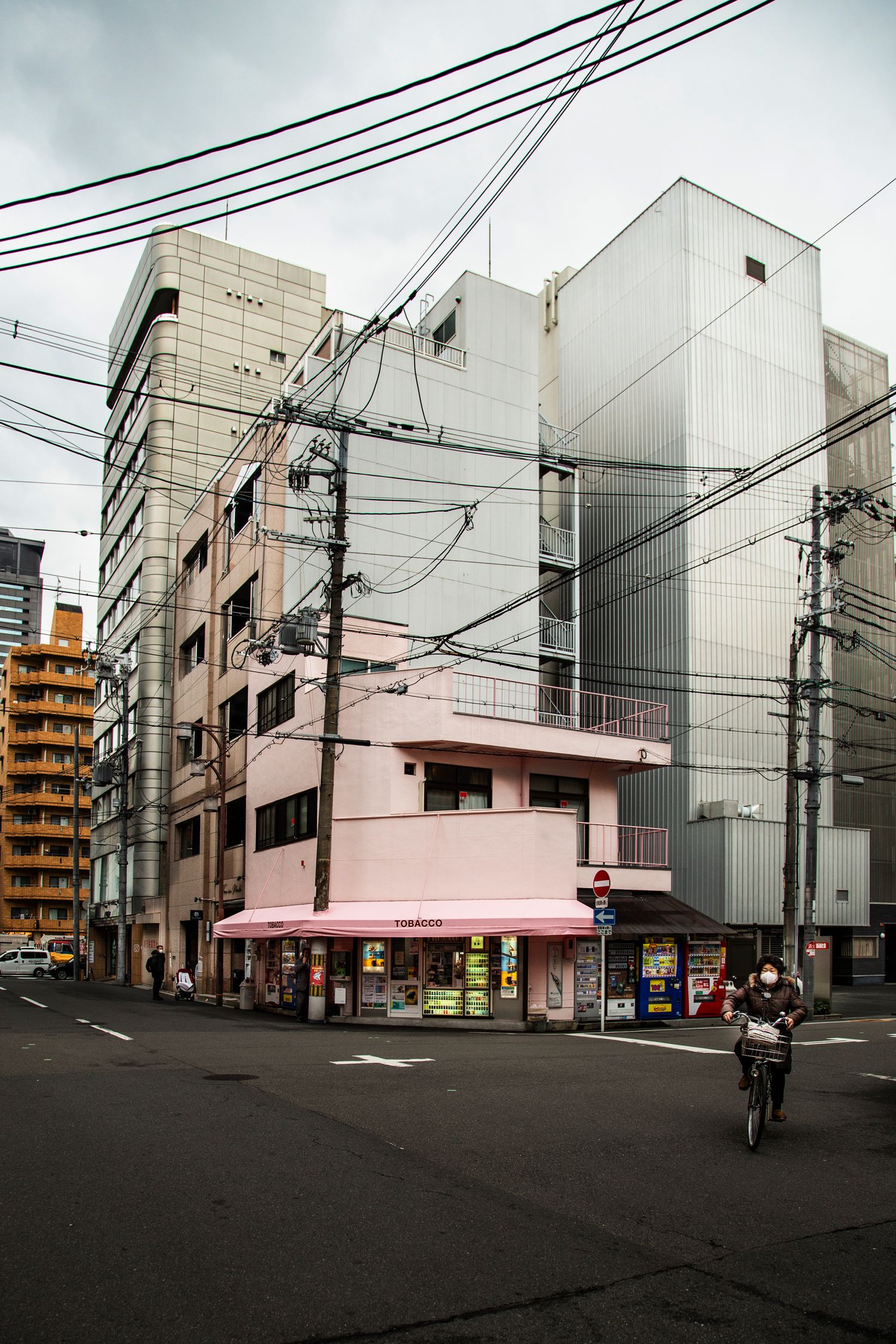 Urban intersection with pink and white buildings and utility poles against cloudy sky.