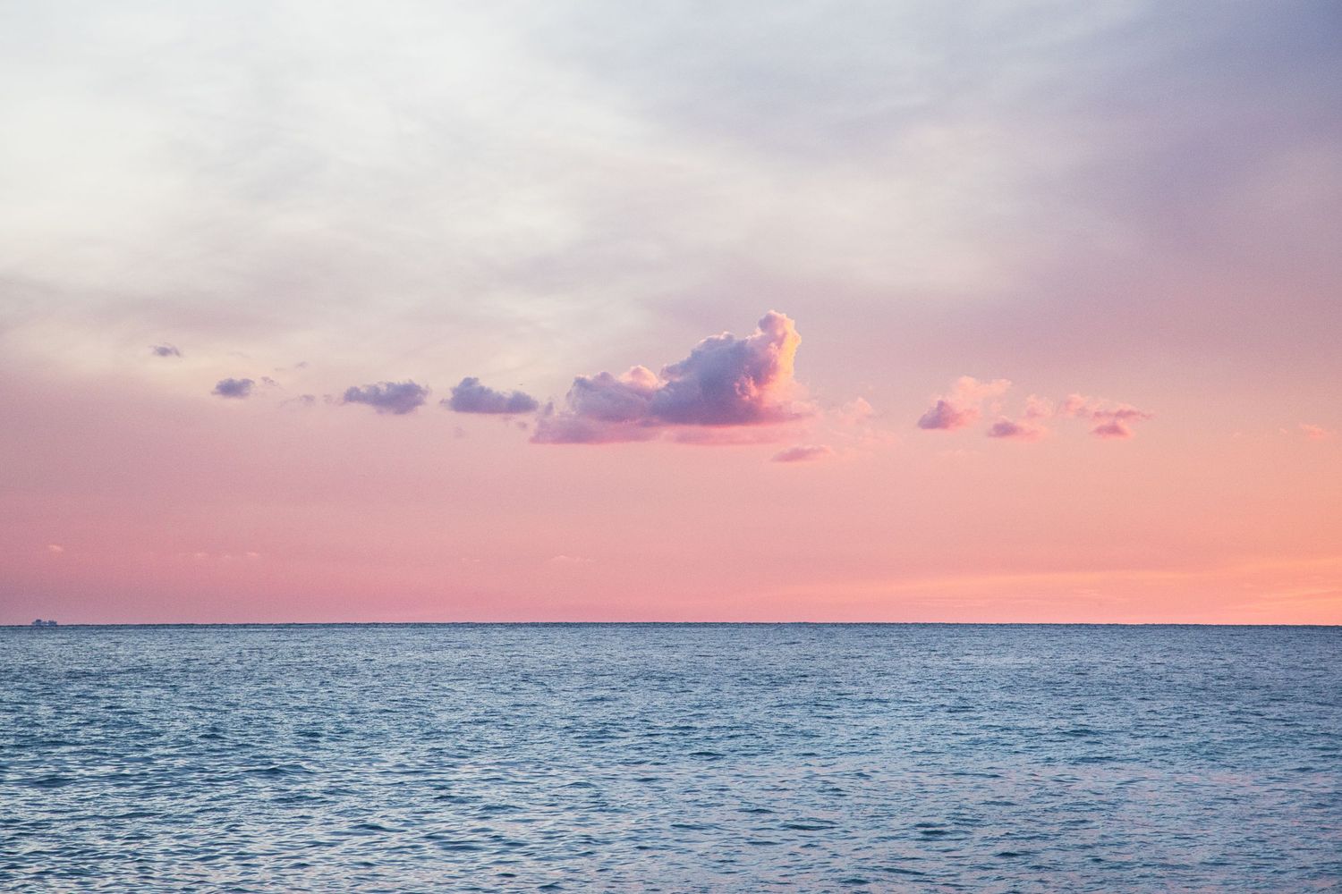 Serene ocean view at sunset with pink and purple clouds reflecting over calm blue water.