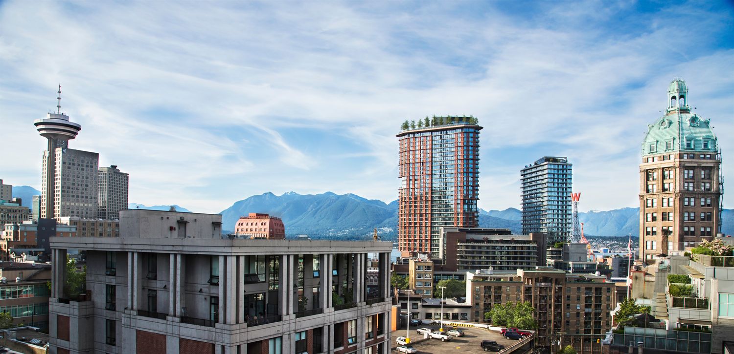 Urban skyline of Vancouver with modern skyscrapers against mountain backdrop and blue sky.