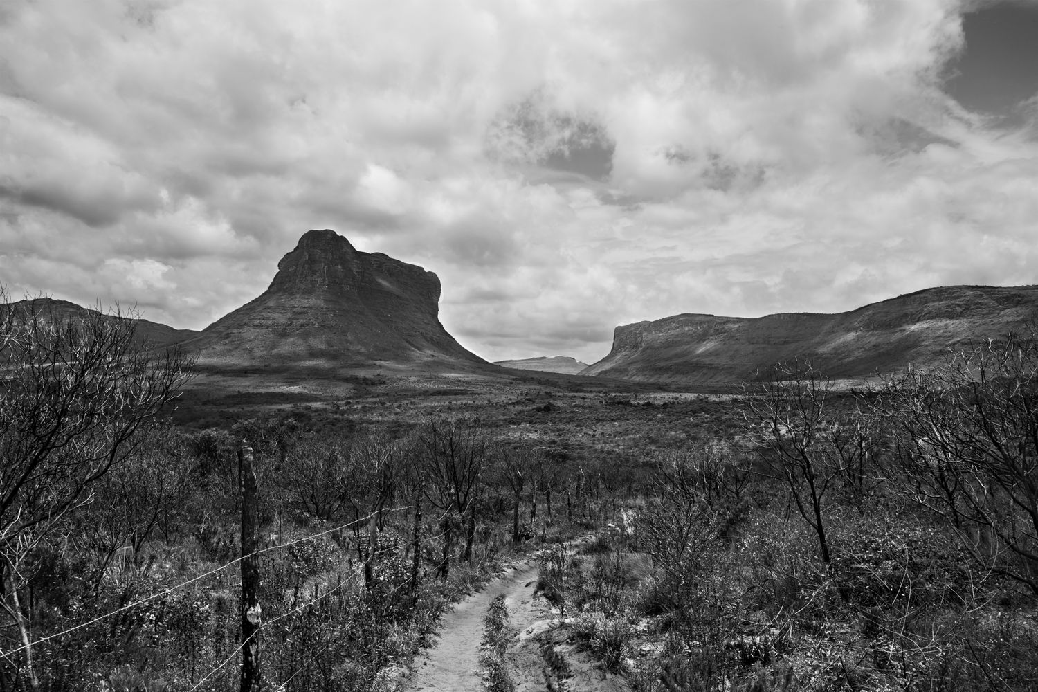 Panoramic black and white mountain landscape with dramatic cloud formations and winding path.