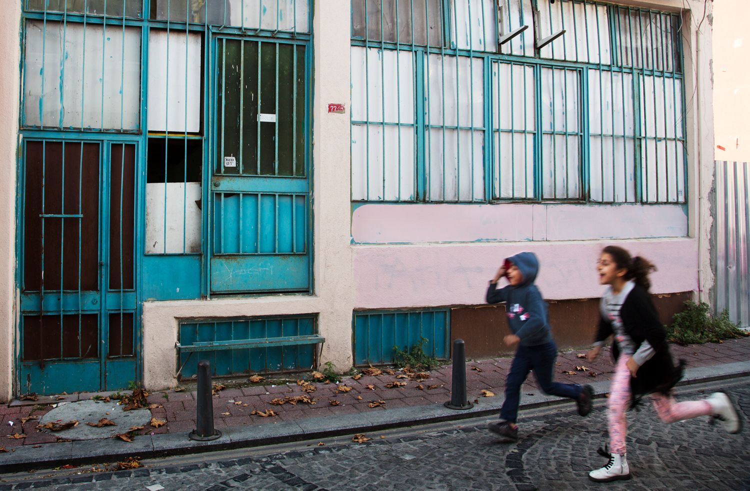 People walking down a narrow urban street lined with white buildings and turquoise doors.