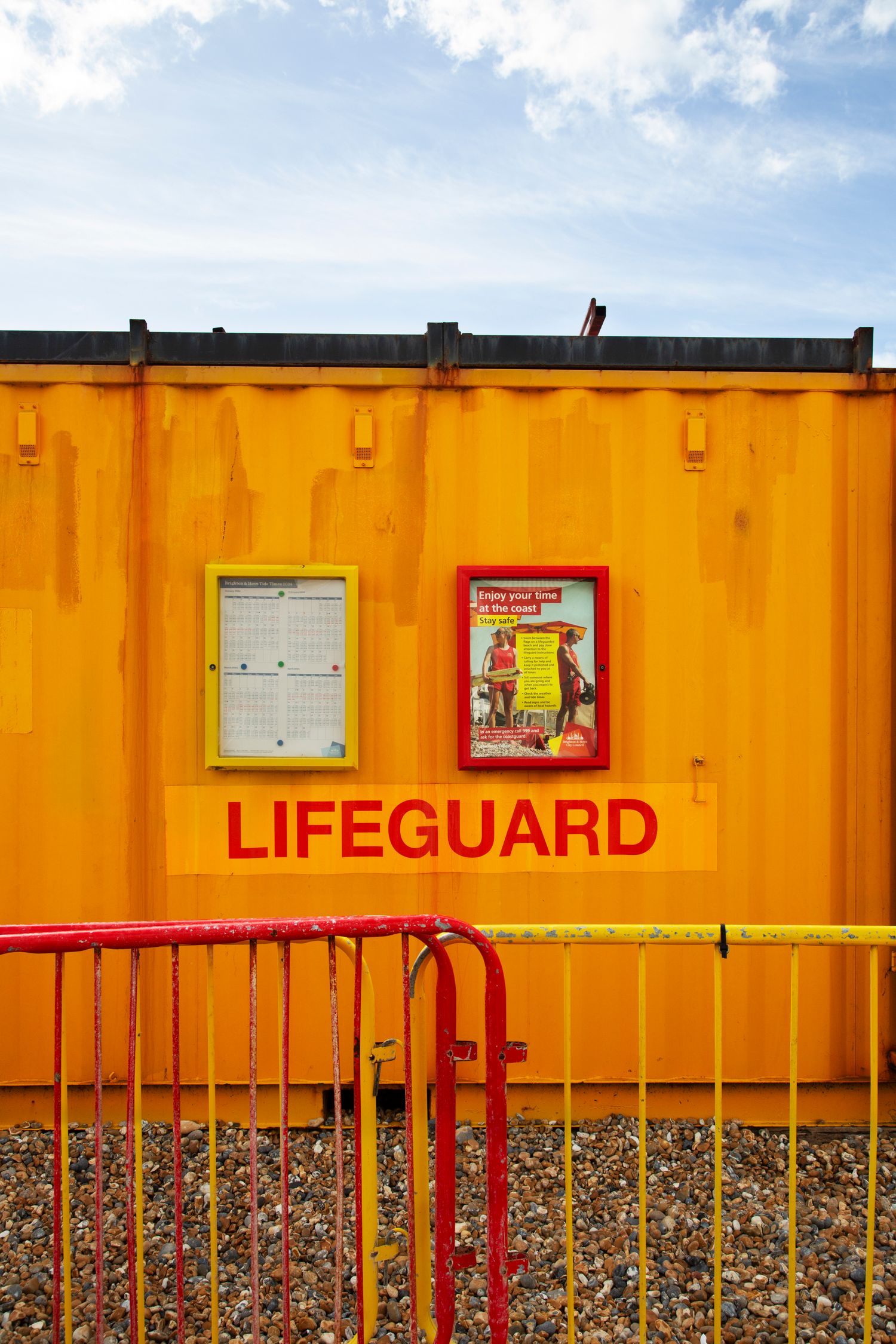 Bright yellow lifeguard station with red railing against blue sky.