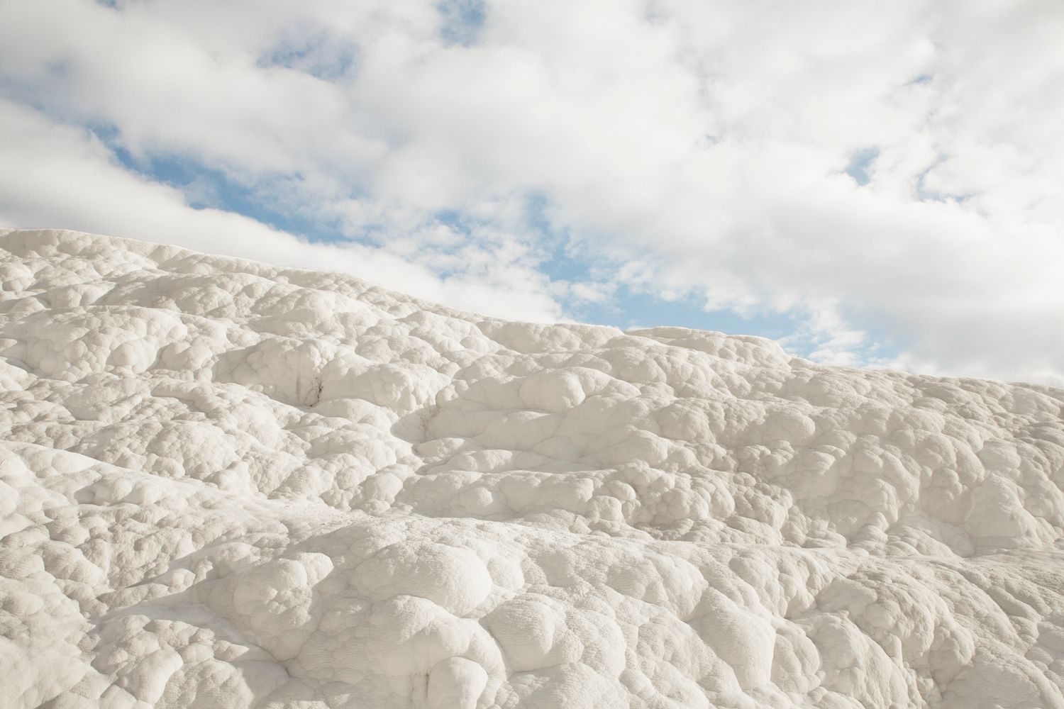 Snow-covered mountain peaks under bright clouds and blue sky.
