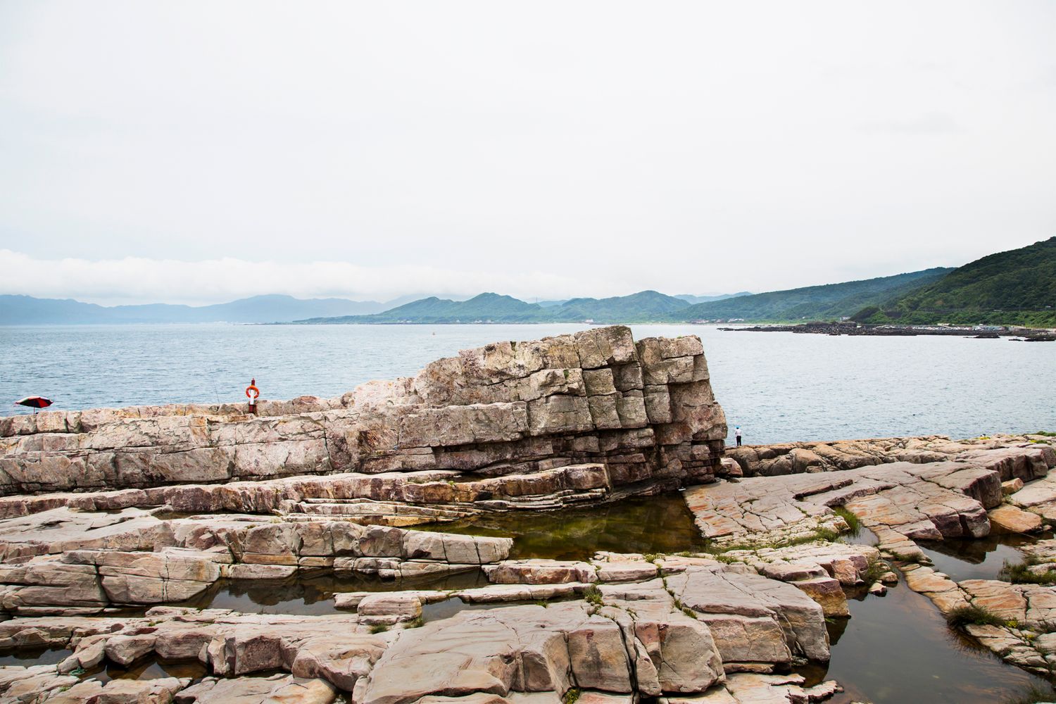 Rocky coastal outcrop with layered limestone formations overlooking a serene bay.