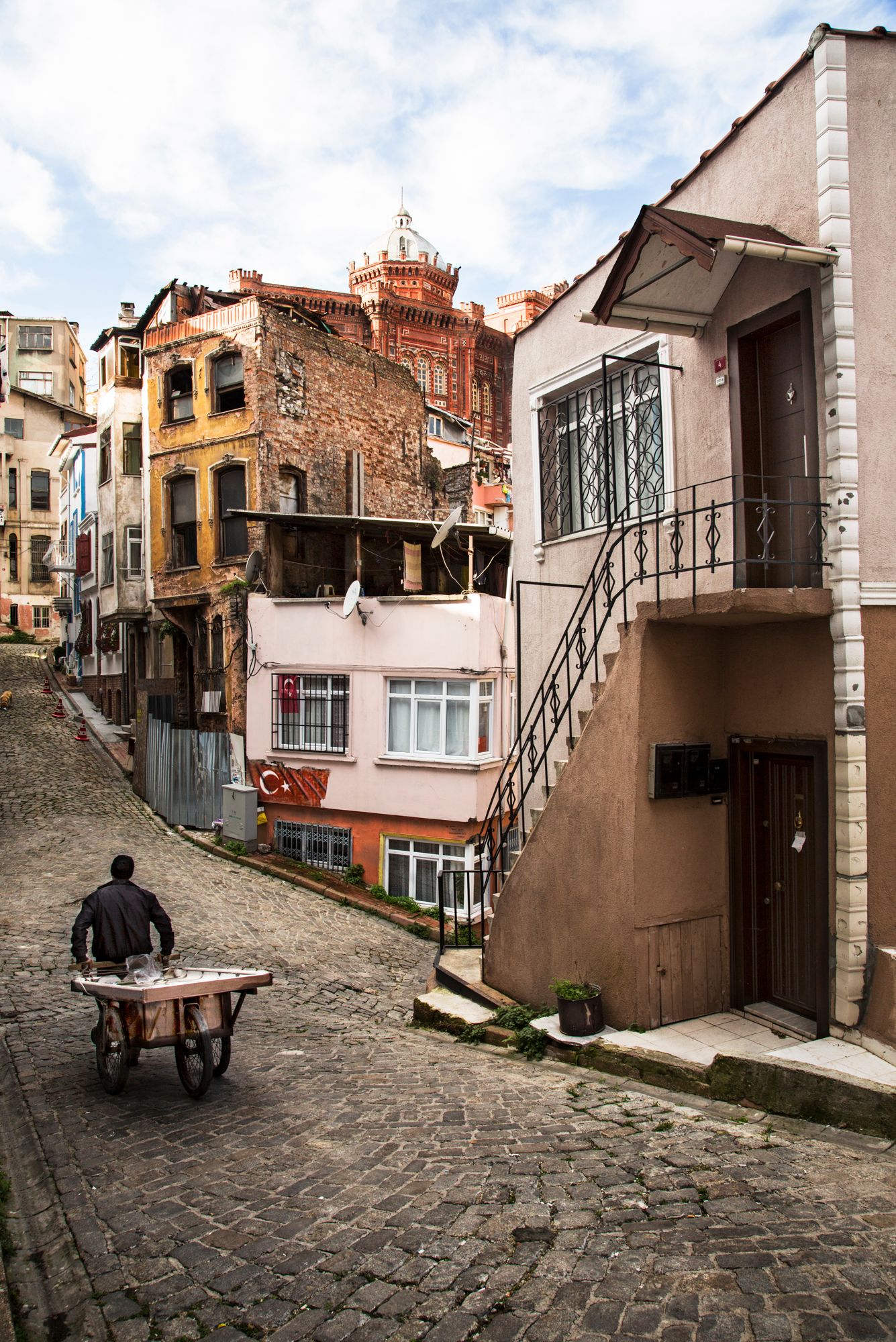 Narrow cobblestone street between old residential buildings with stone facades and stairs.