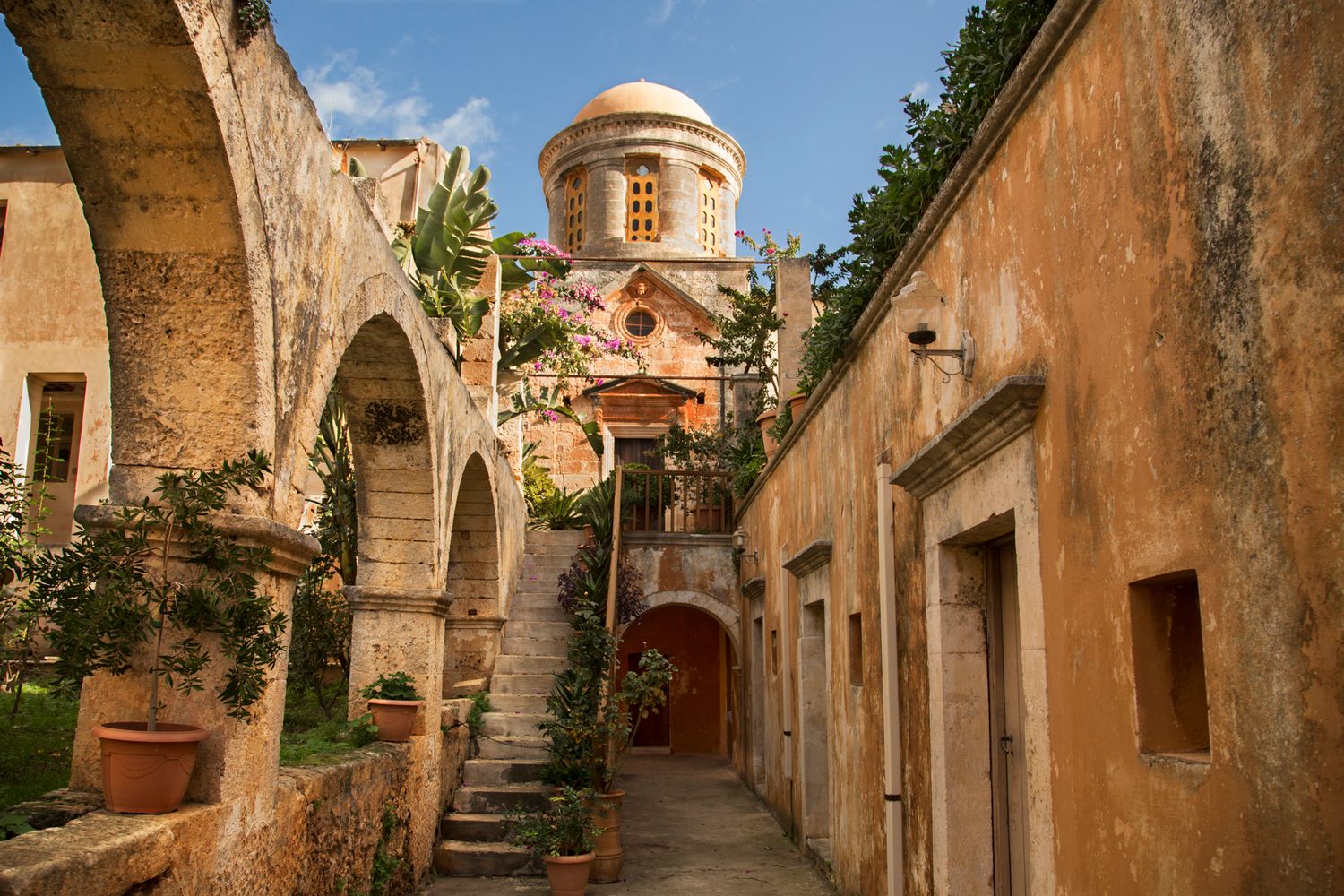 Ancient Mediterranean alleyway with stone archways and domed church in warm sunlight.