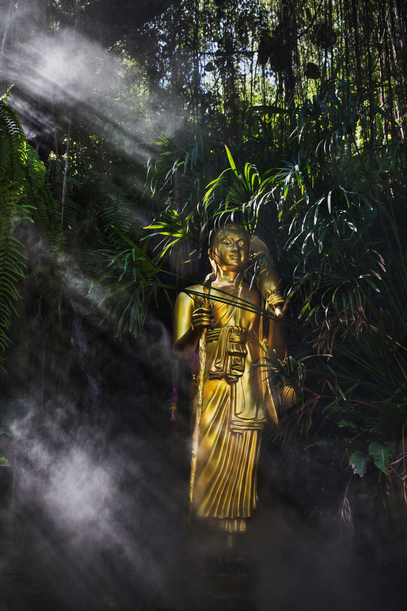Golden Buddhist statue surrounded by mist and bamboo forest with dramatic light rays.