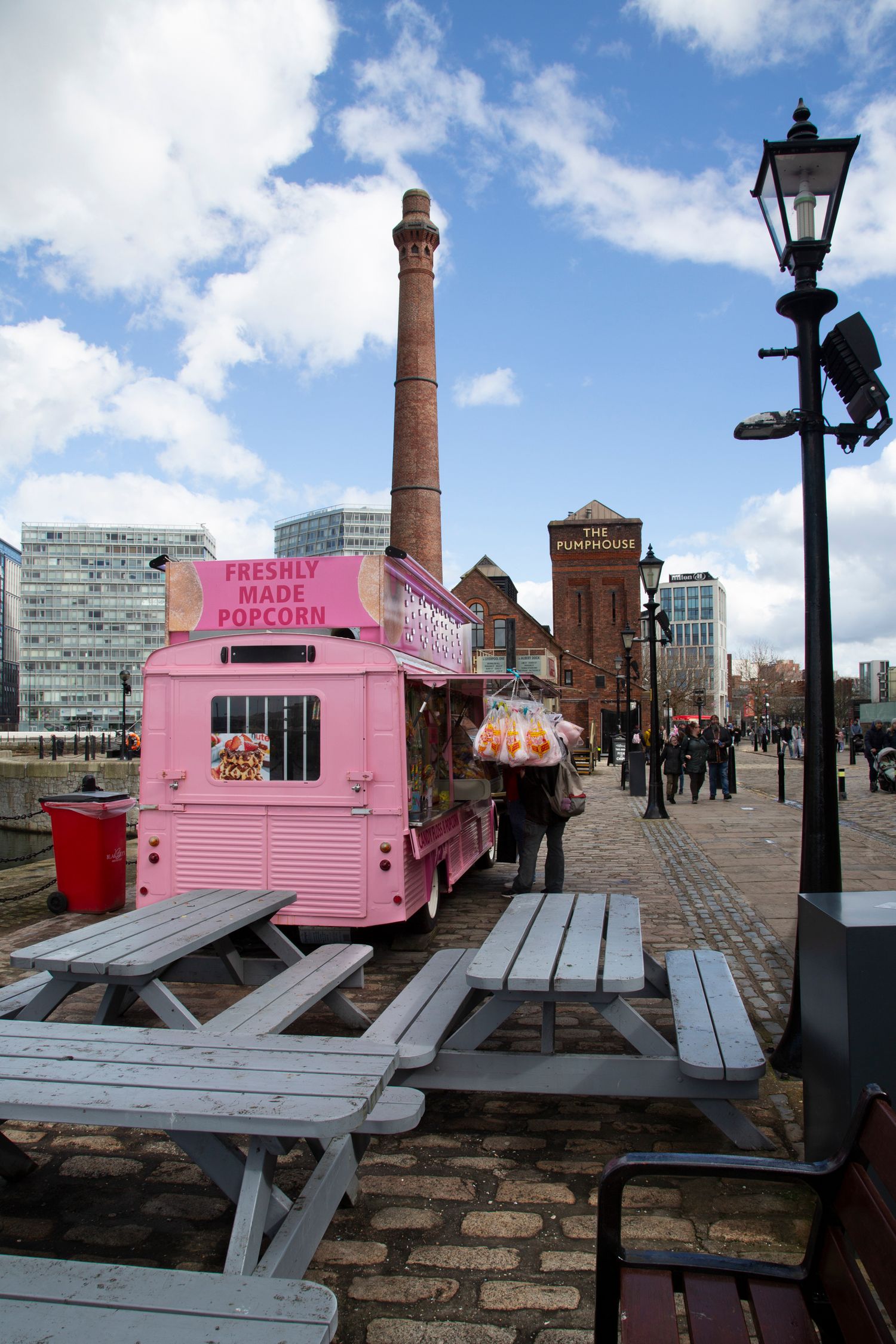 Pink food stand and picnic tables on a dock with industrial buildings and a brick chimney in the background.