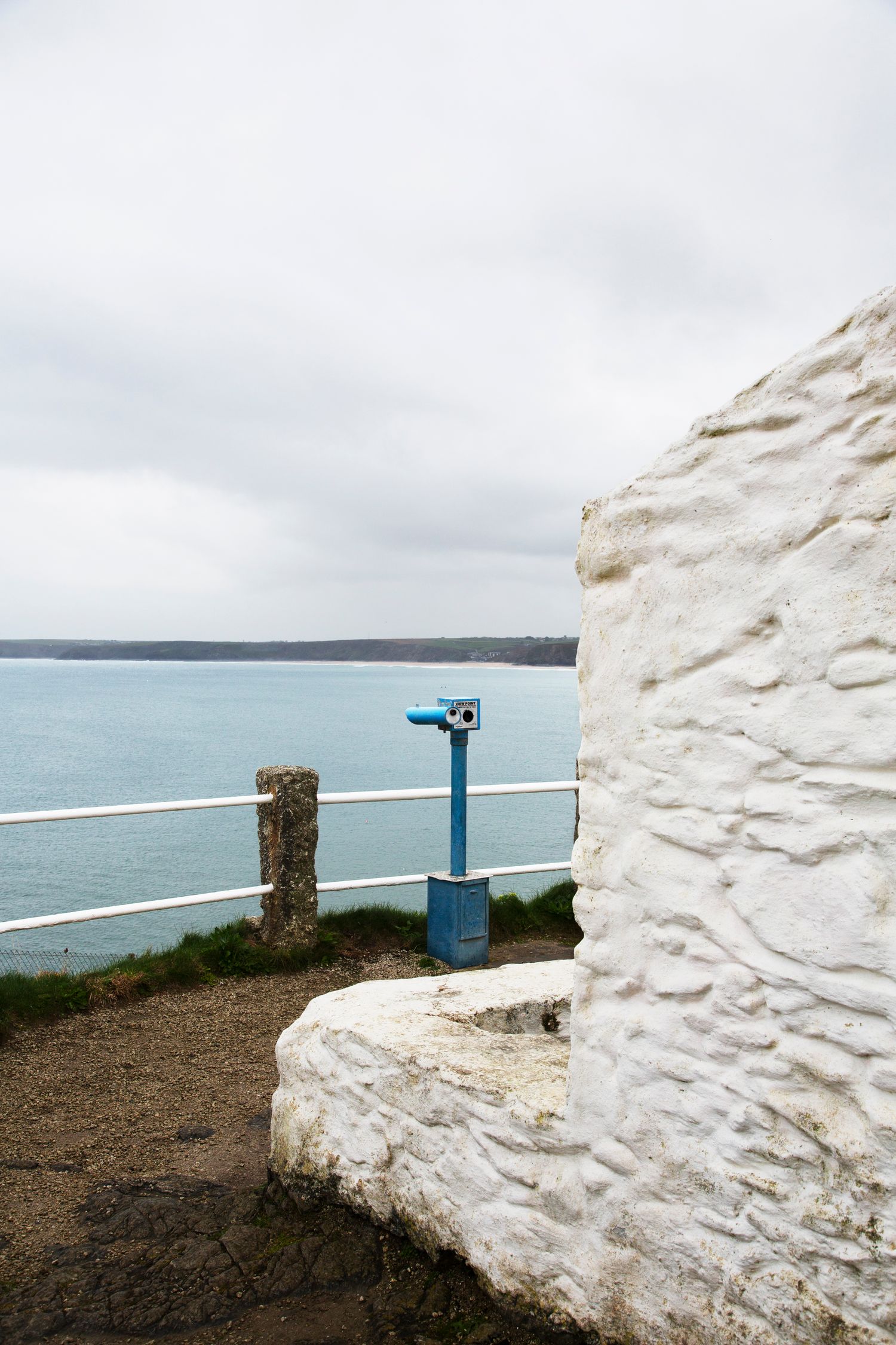 Blue coin-operated viewfinder next to whitewashed wall overlooking coastal waters.