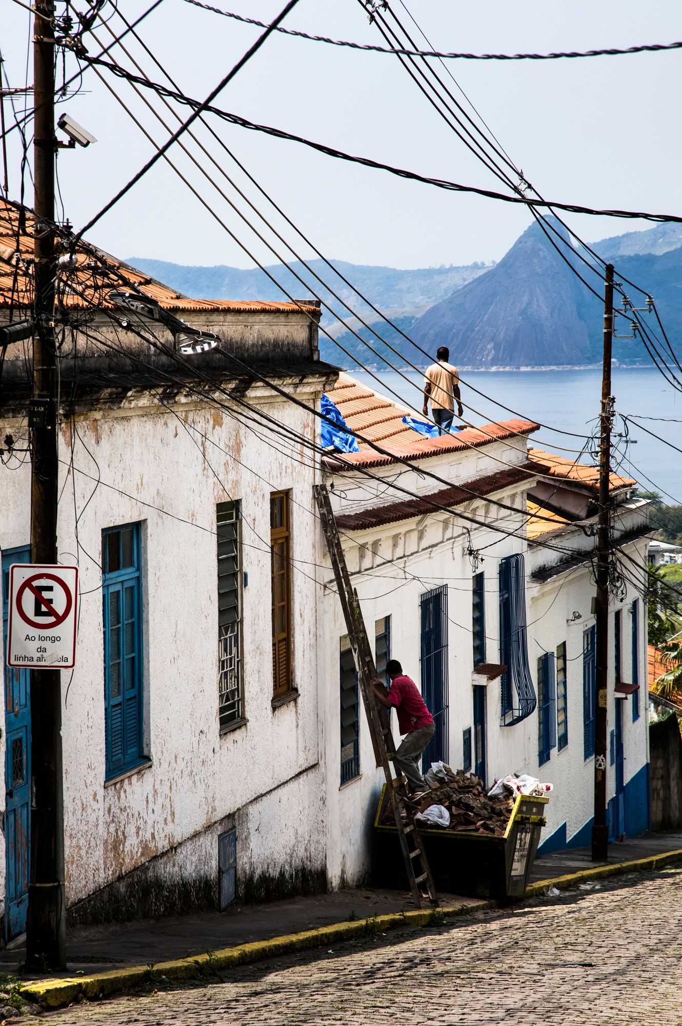 Cobblestone street lined with white colonial houses and power lines in a Brazilian hillside neighborhood.