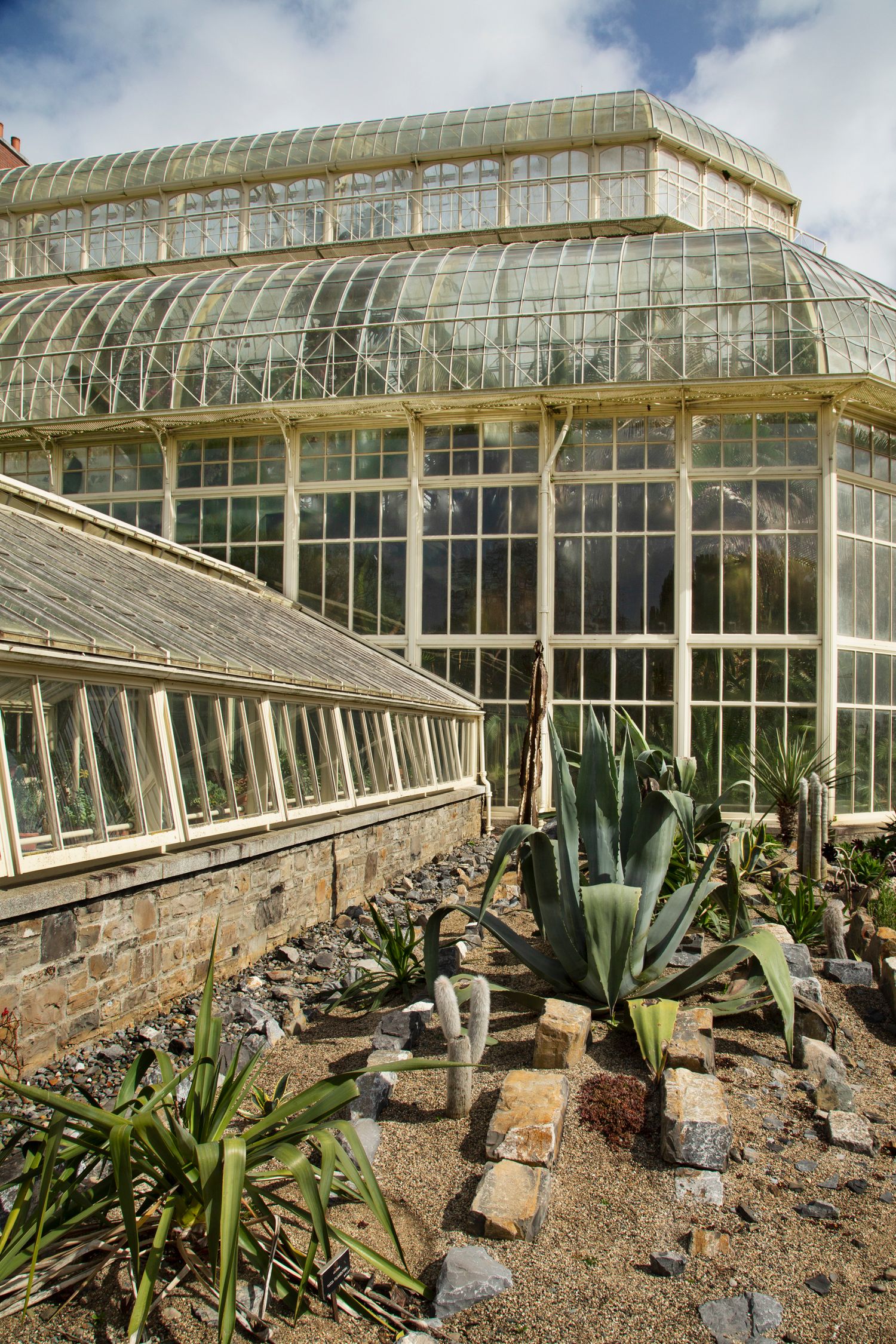 Large Victorian greenhouse with succulent garden and rock landscaping in foreground.