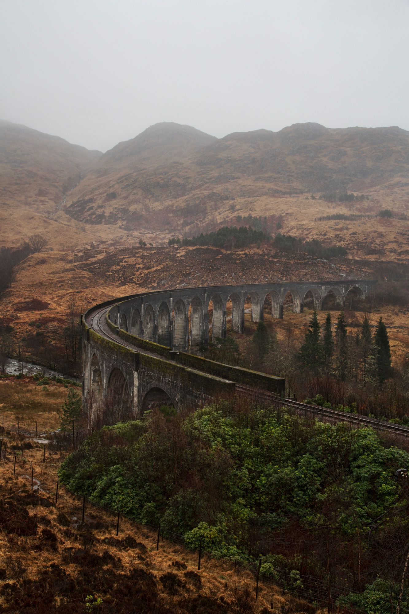 A scenic view of the Glenfinnan Viaduct railway bridge in the Scottish Highlands on a misty autumn day.