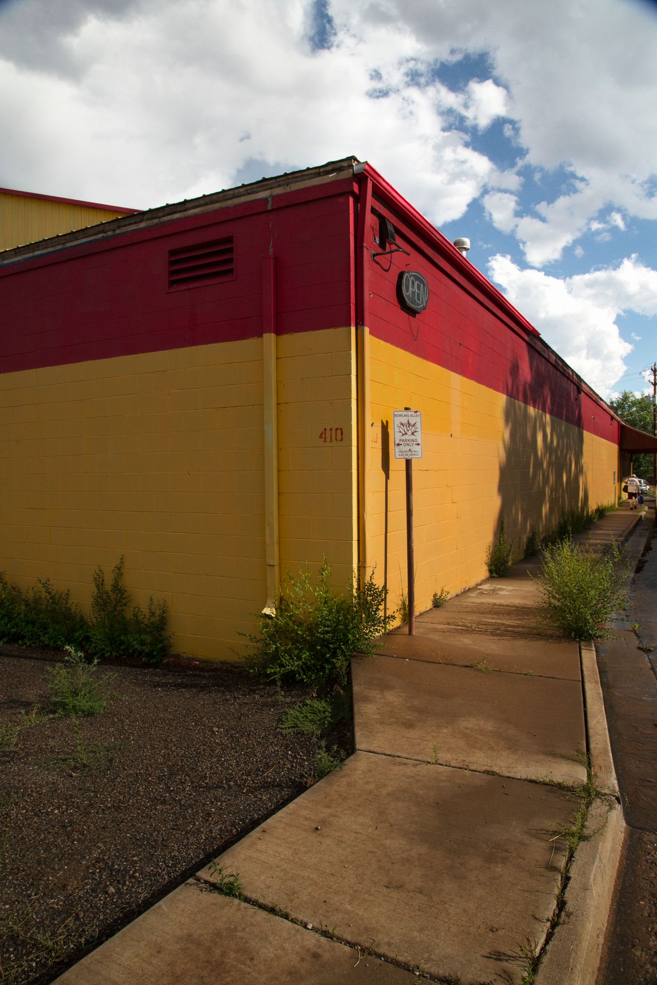 A series of connected red and yellow industrial buildings with sloped roofs against a blue cloudy sky.