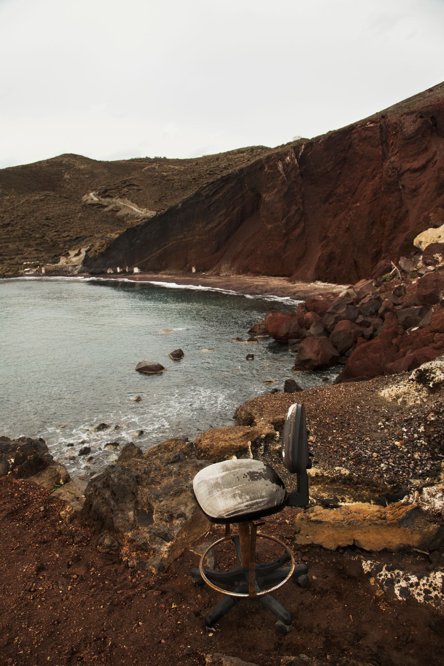 Aerial view of a rugged coastline with red cliffs and a small road winding along the edge of the sea.