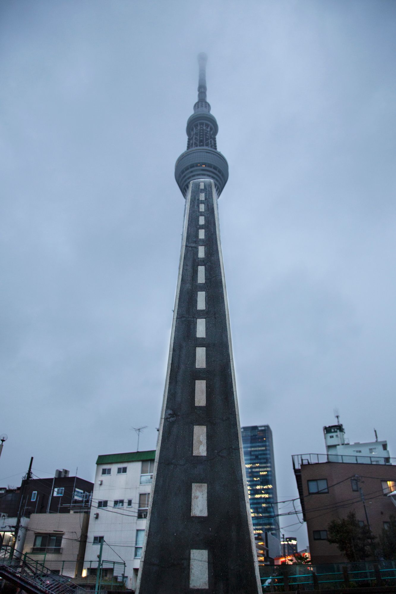 Dark industrial tower silhouetted against cloudy sky in urban setting.