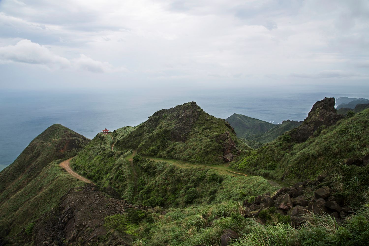 Rugged mountain ridge trail with sweeping views of green peaks and distant ocean horizon.