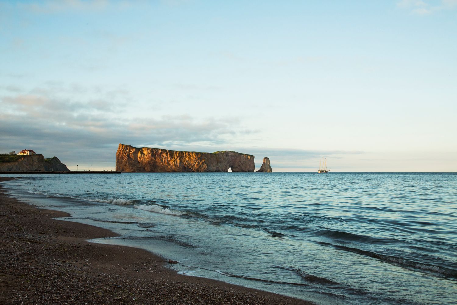 Dramatic red rock cliffs and sea arch formation along a beach at dusk.