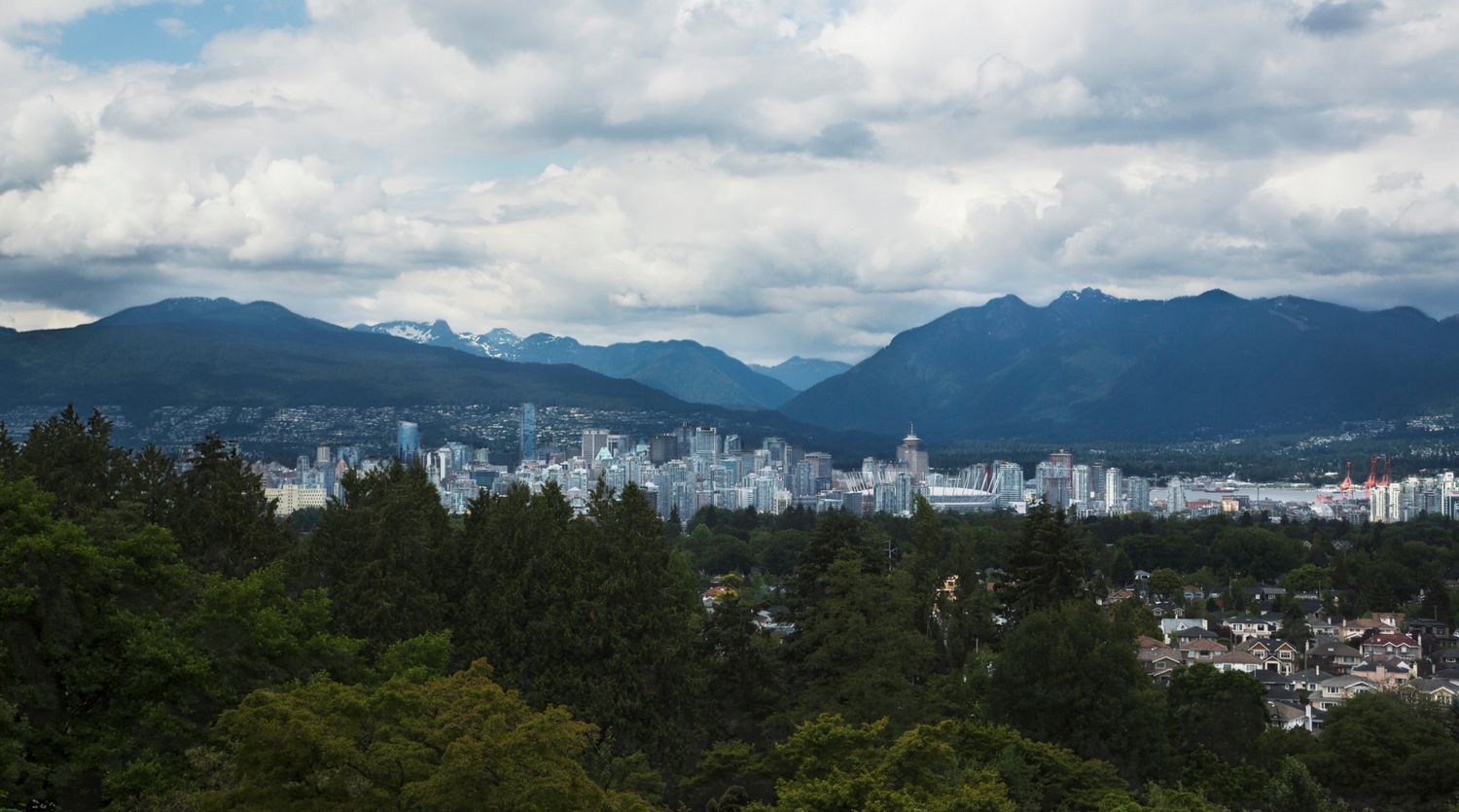 Panoramic cityscape with mountains in the background under partly cloudy skies.
